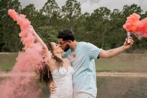 Couple throws pink smoke bombs while dancing and celebrating in a scenic outdoor setting.