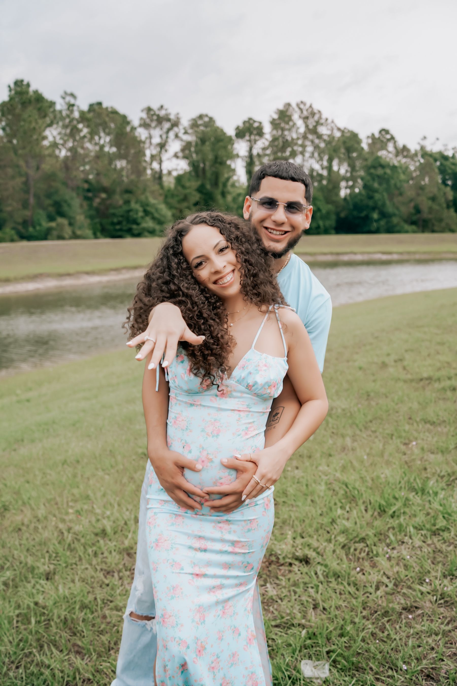 Outdoor maternity photo of couple in light blue attire posing in grassy field.