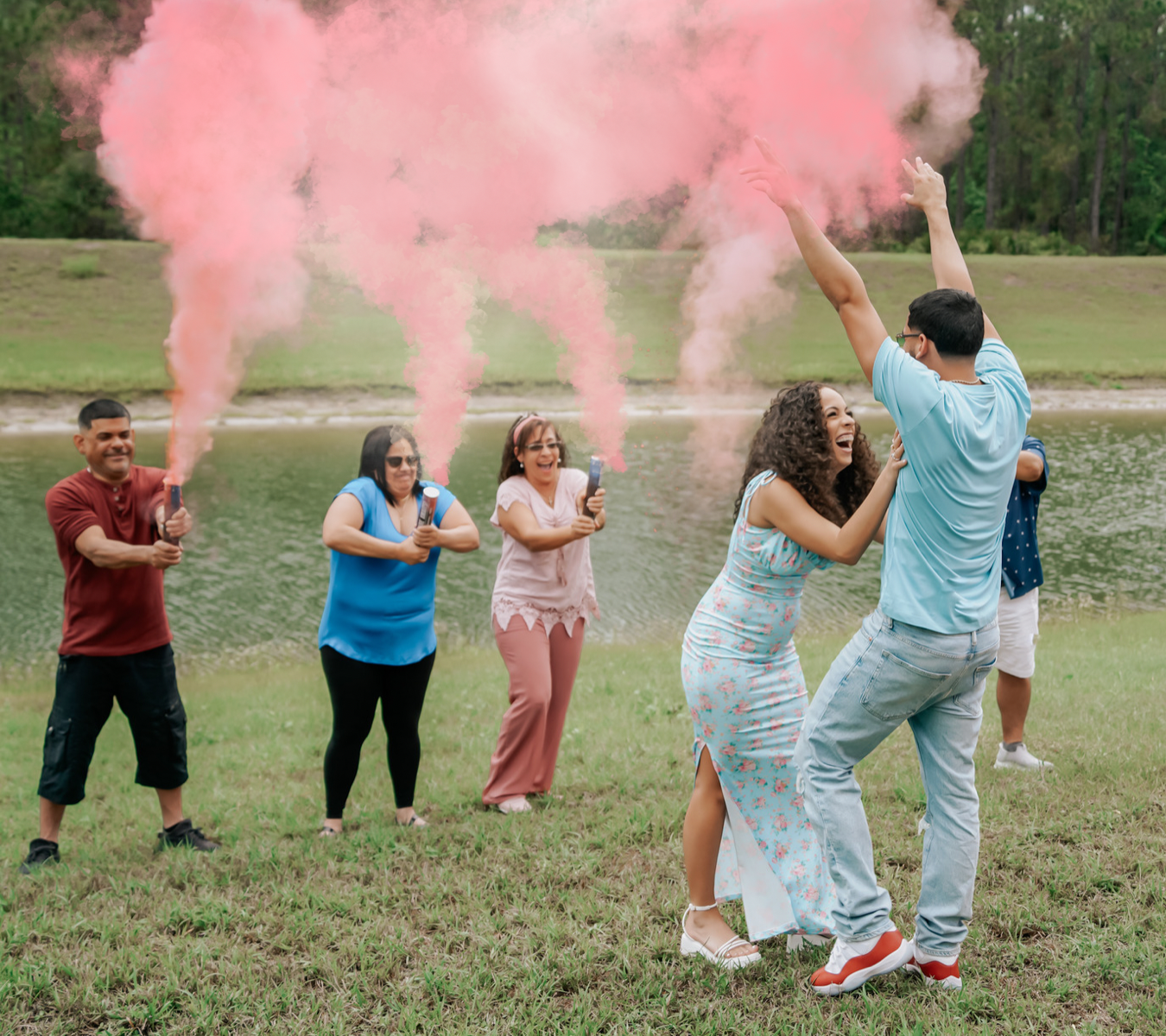 Group celebrates with pink smoke bombs in an outdoor field setting.