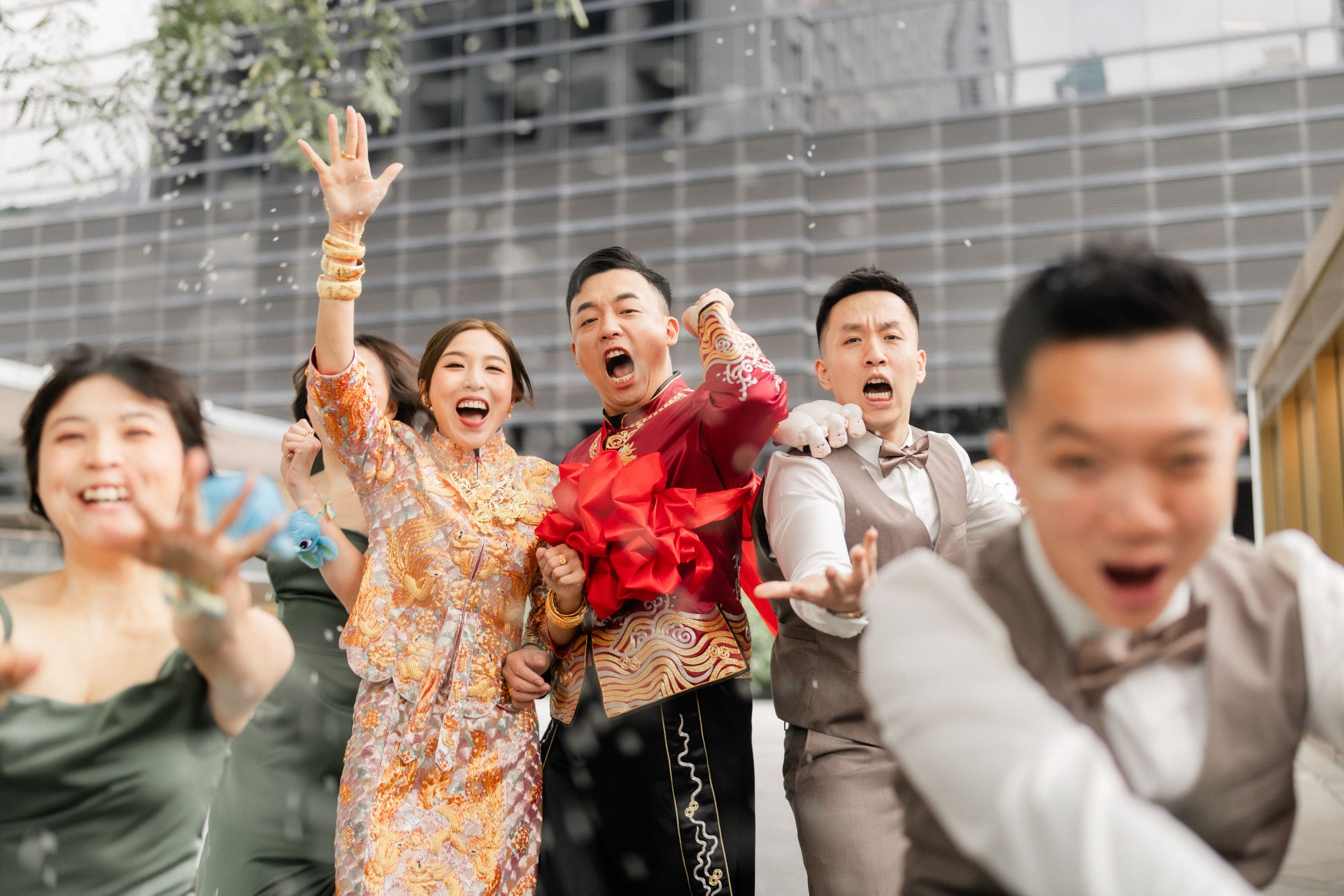 Excited Chinese wedding party celebrates outdoors with confetti in traditional and formal attire.
