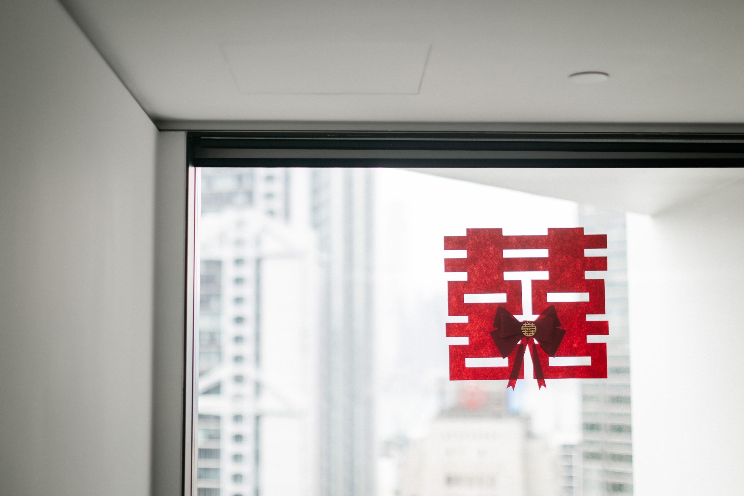 Red double happiness Chinese wedding symbol decoration on a window with city skyline in background.
