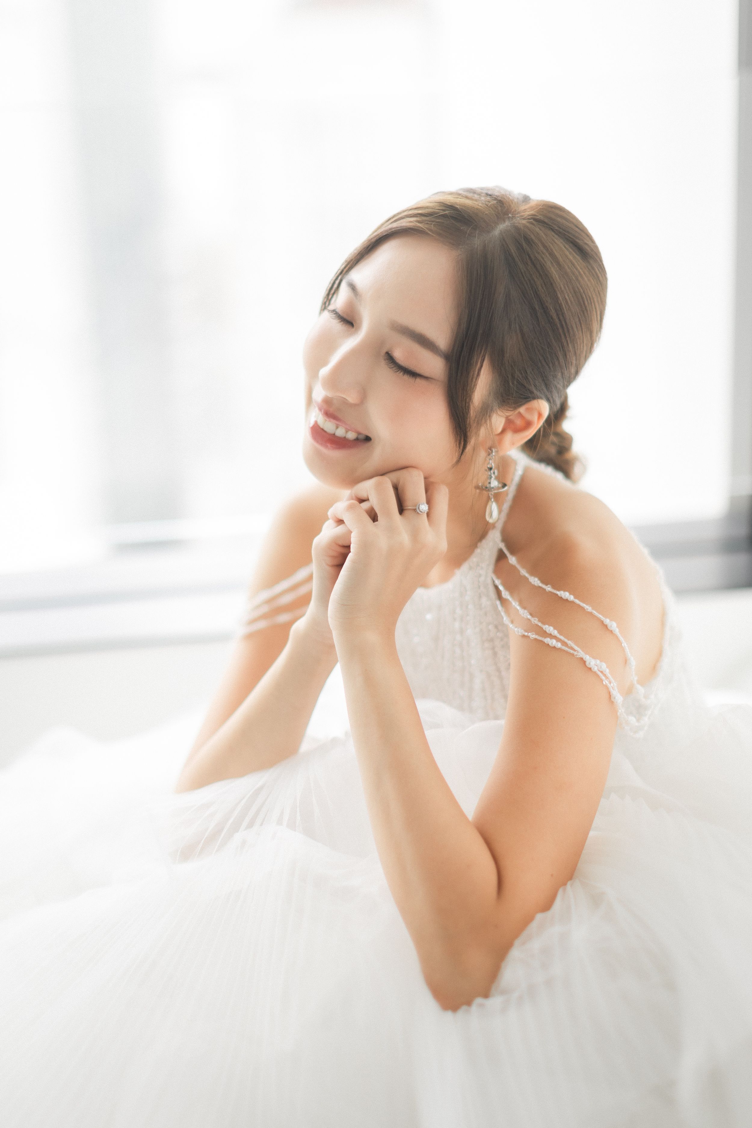 Beautiful Asian bride in a white beaded wedding dress smiling with eyes closed wearing drop earrings.