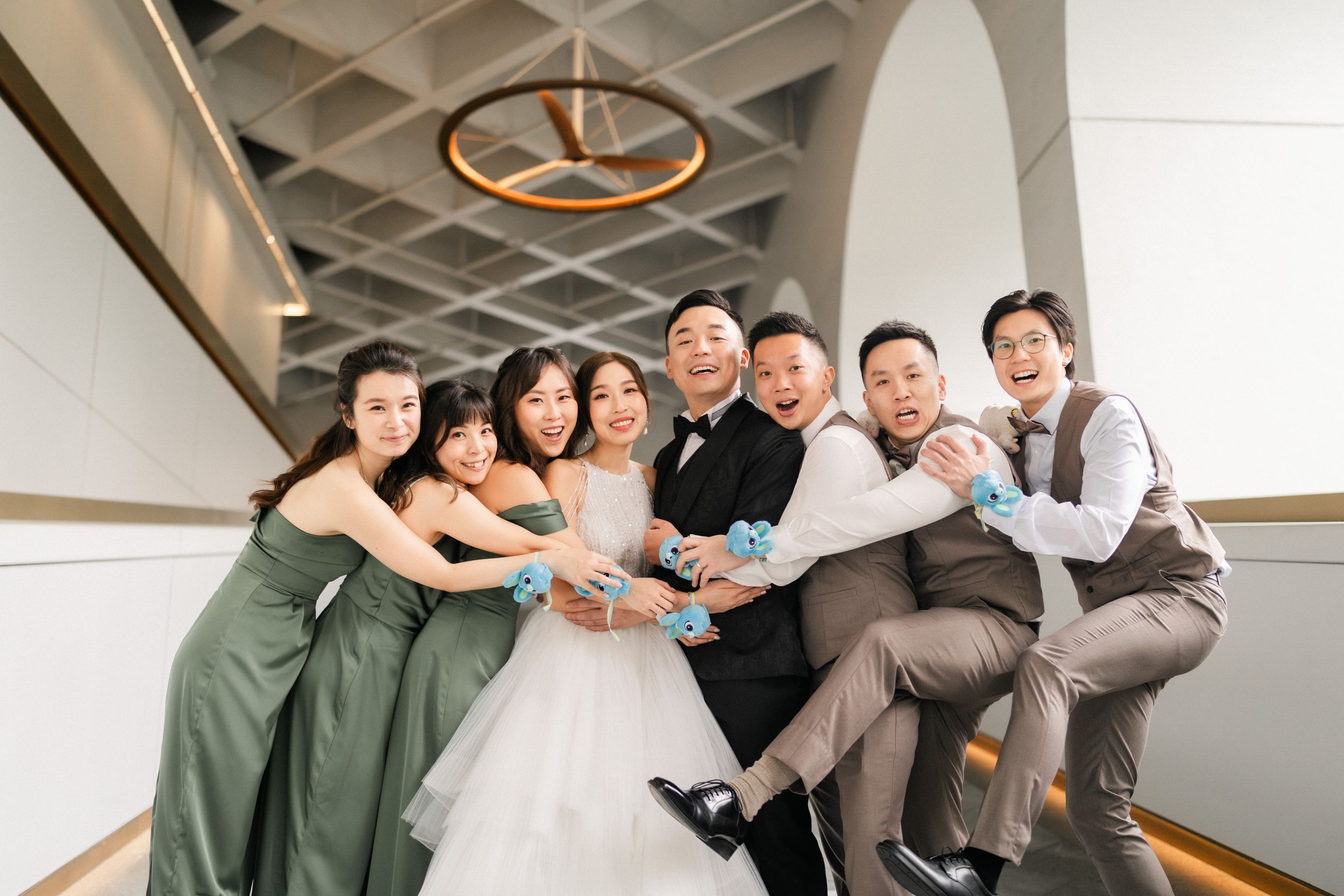 Wedding party group photo with bride, groom, bridesmaids in sage green and groomsmen laughing together.