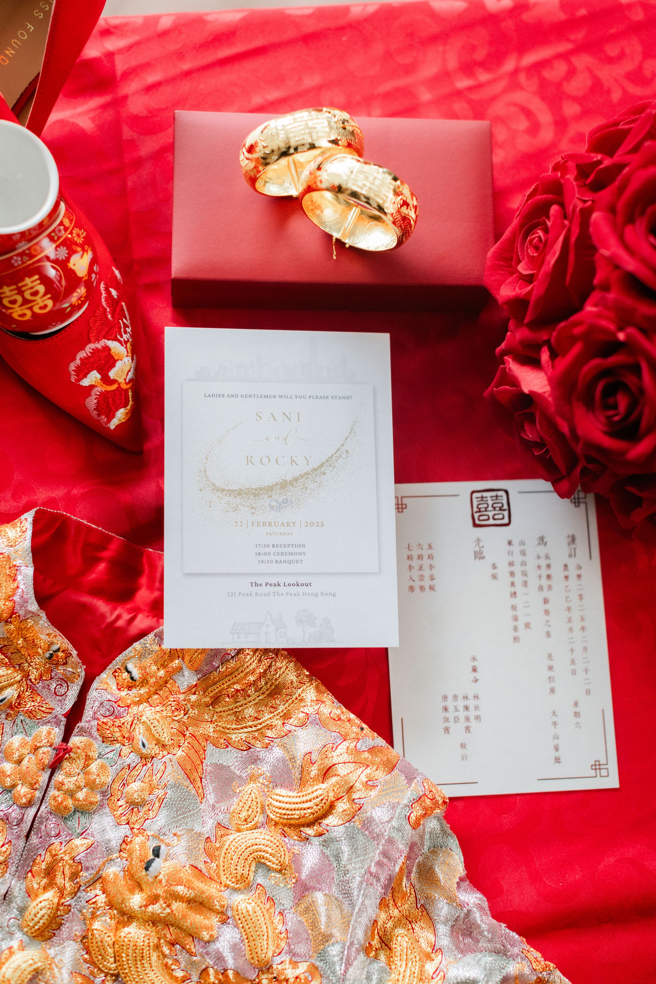 Chinese wedding flat lay with red gift box, gold jewelry, invitation, and embroidered qipao.