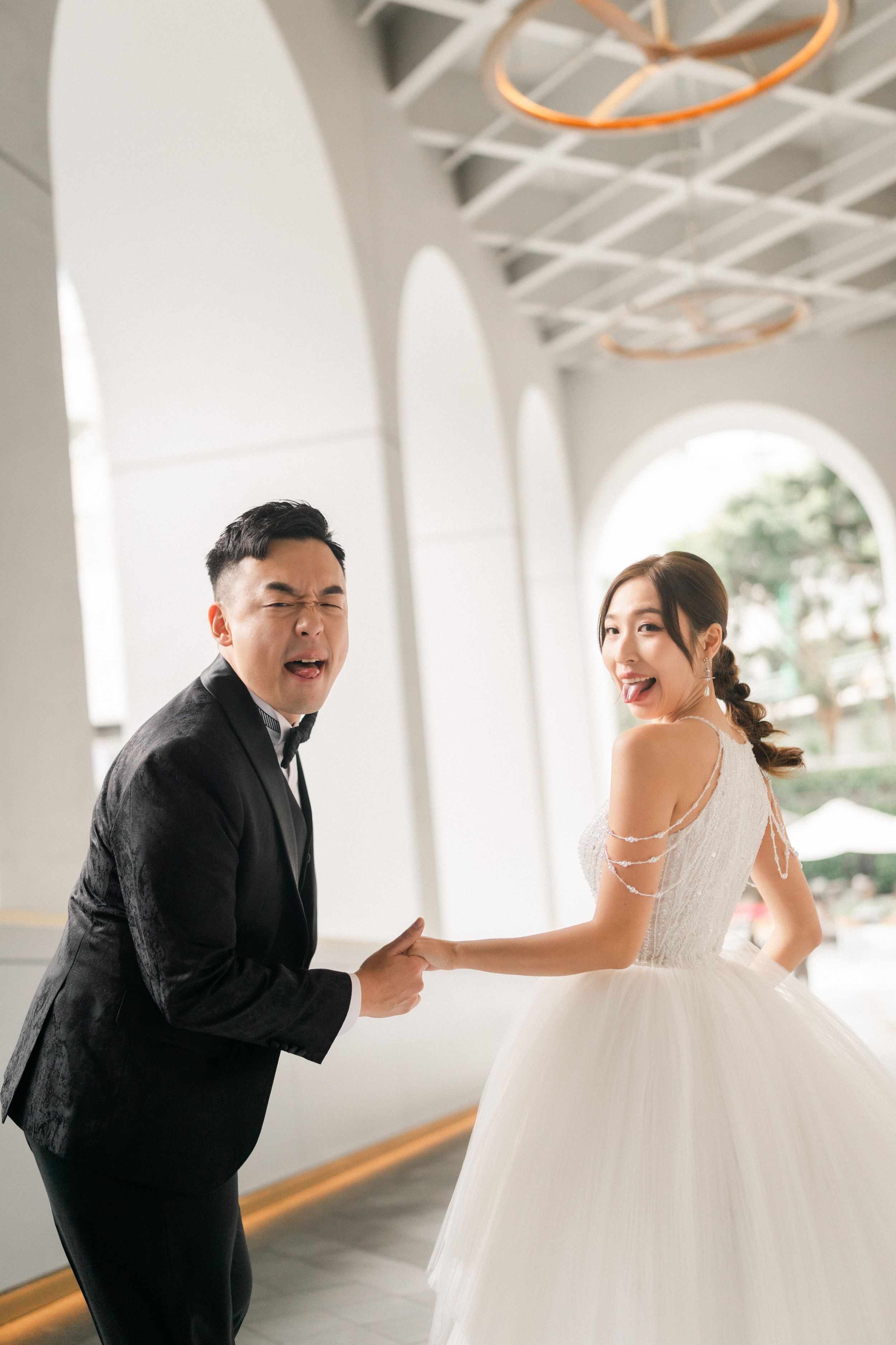 Laughing bride and groom share a playful moment dancing together in bright white arched wedding venue.