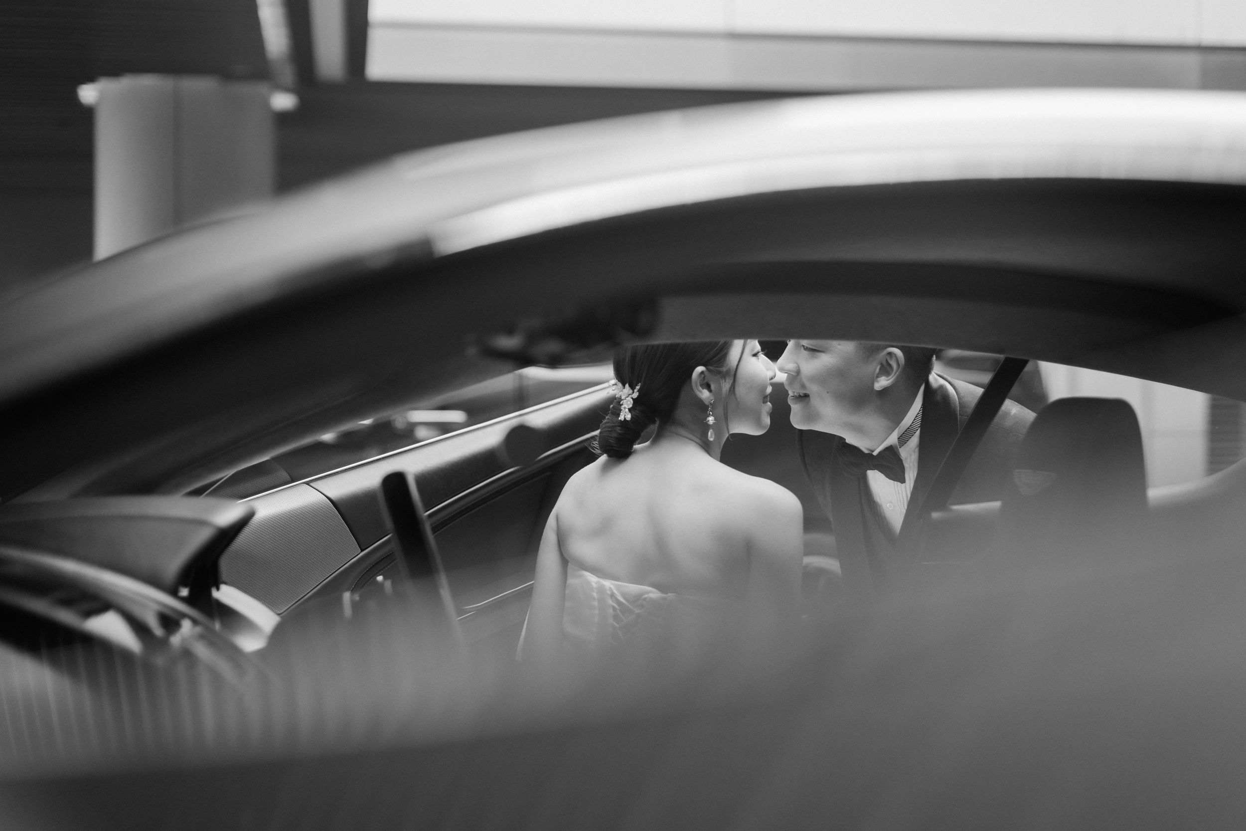 Black and white intimate photo of bride and groom kissing inside a luxury wedding car.