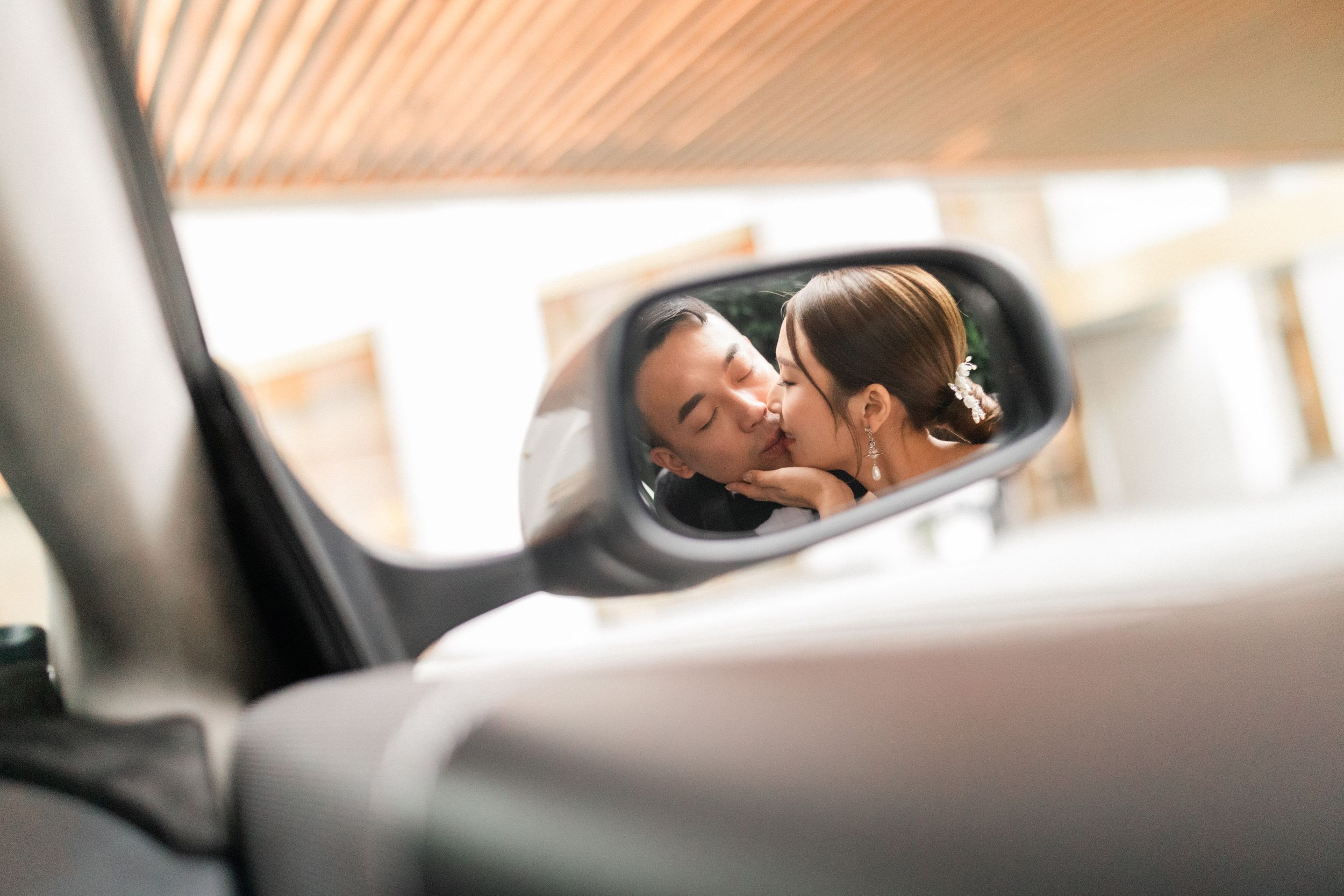 Two people sharing a kiss reflected in a car side mirror.