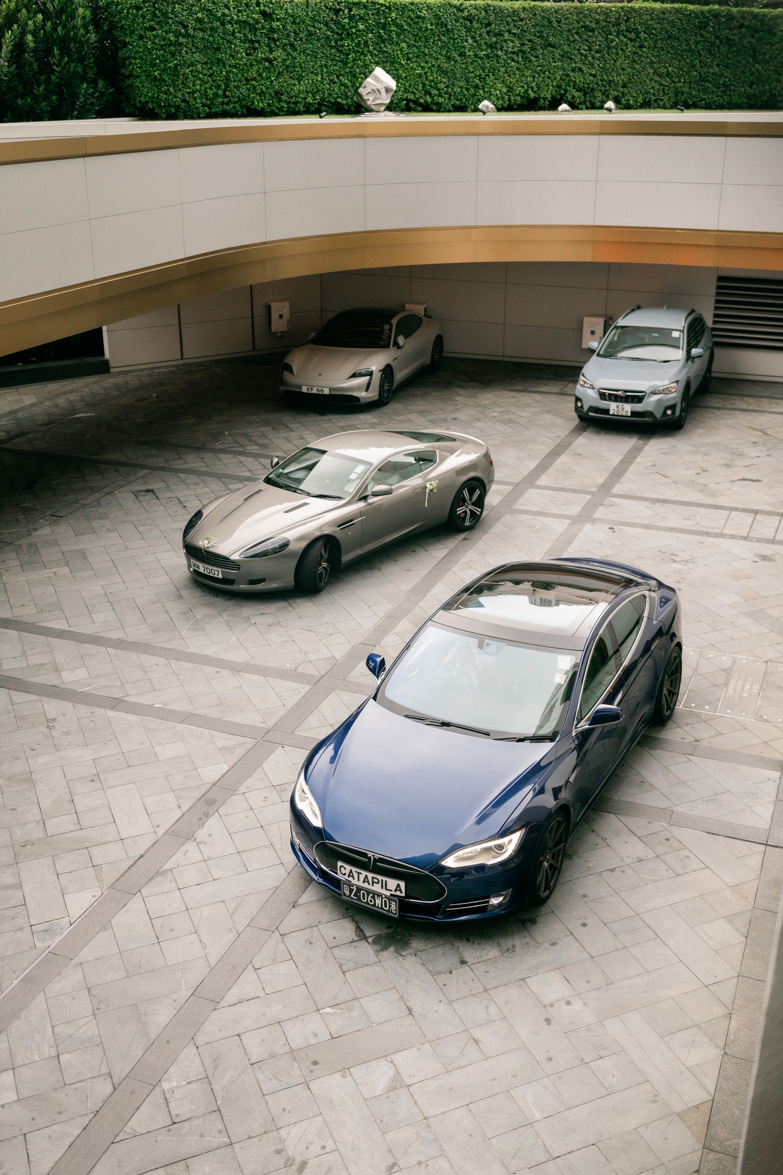 Aerial view of luxury cars including Tesla and Aston Martin parked in an elegant courtyard.