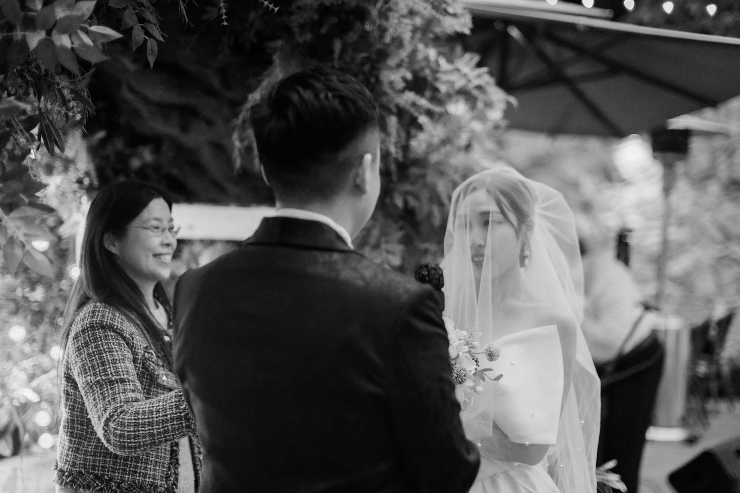 Black and white photo of a bride and groom exchanging vows at an outdoor wedding ceremony.