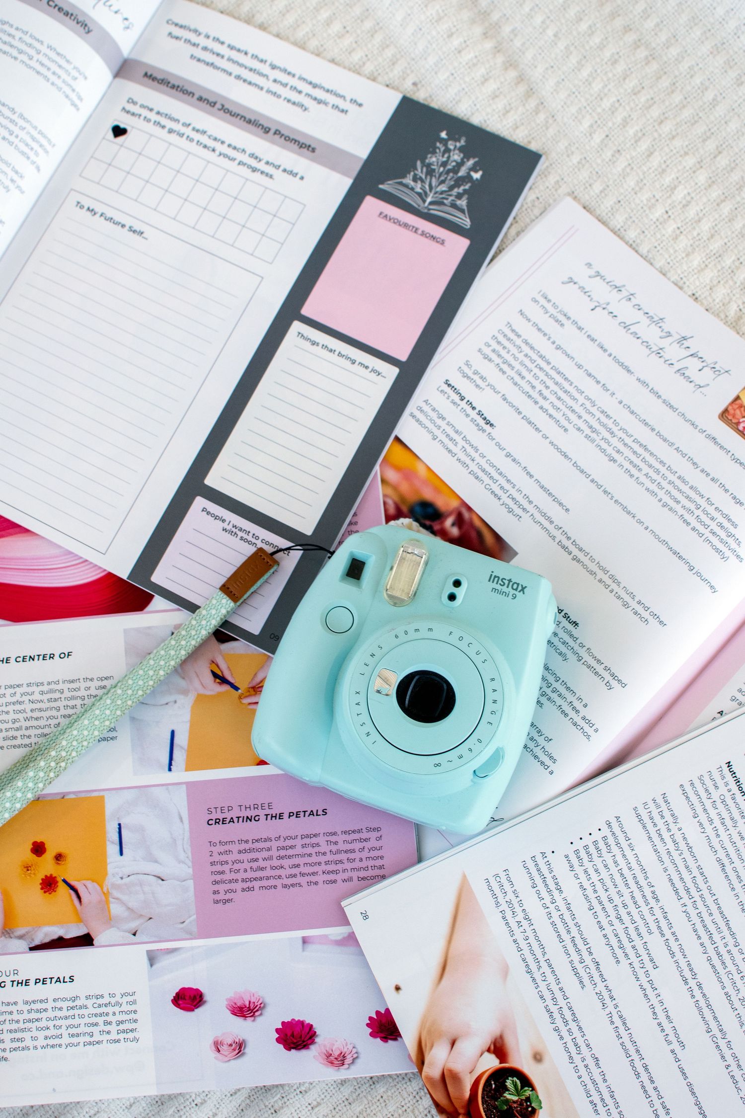 Mint green Instax camera with planning materials and pink sticky notes spread on white surface.