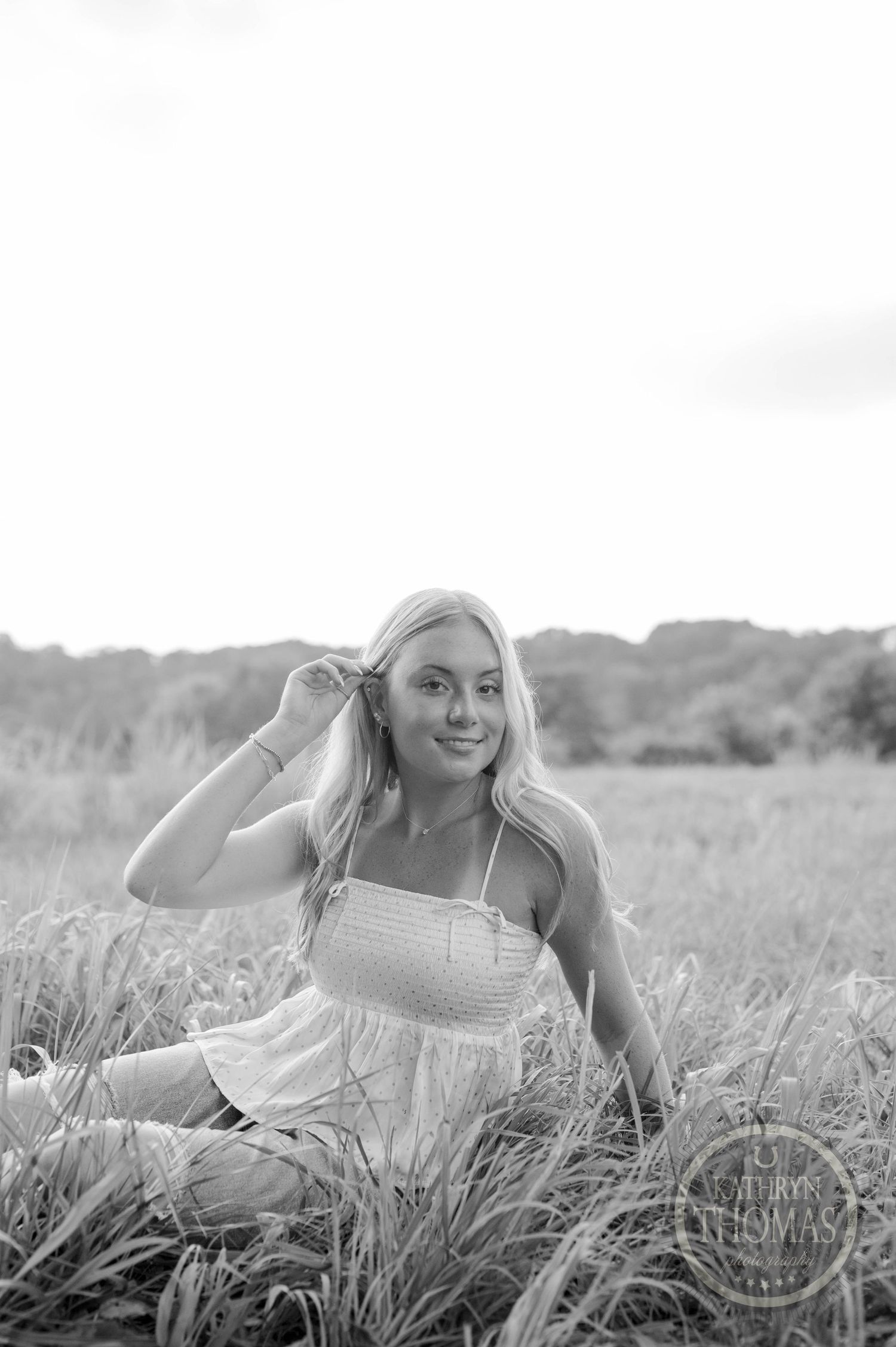 Black and white portrait sitting in tall grass with natural styling.