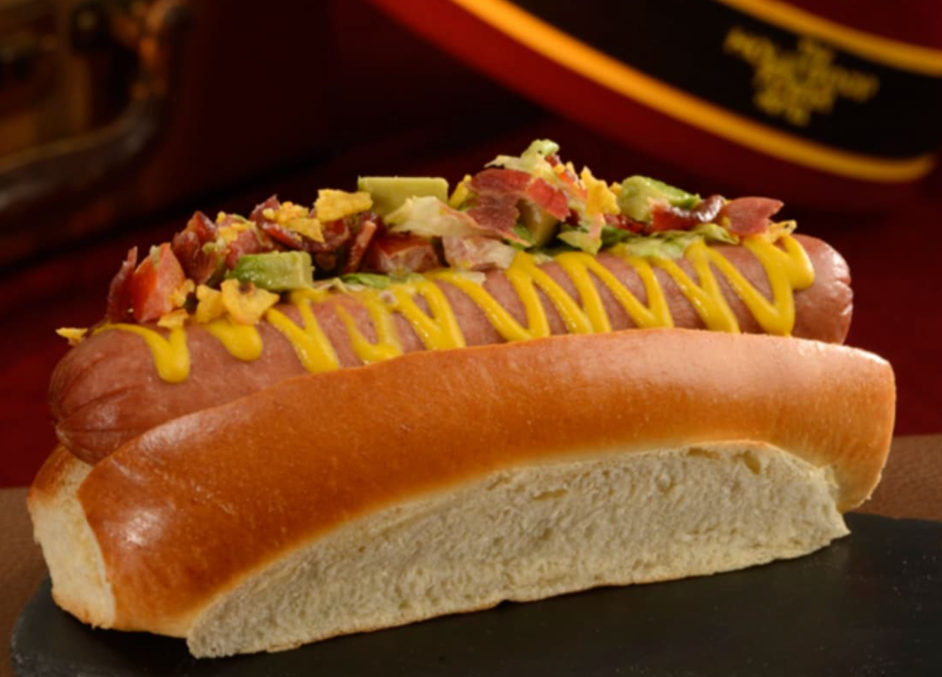 Gourmet hot dog in a toasted bun topped with mustard and fresh toppings.