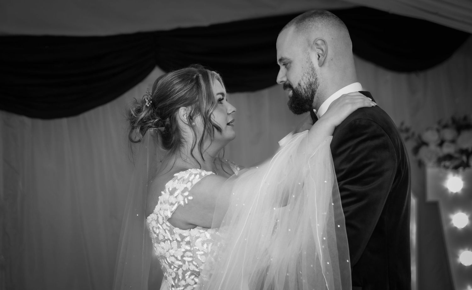 A tender black and white wedding moment captured under draped fabric decor.