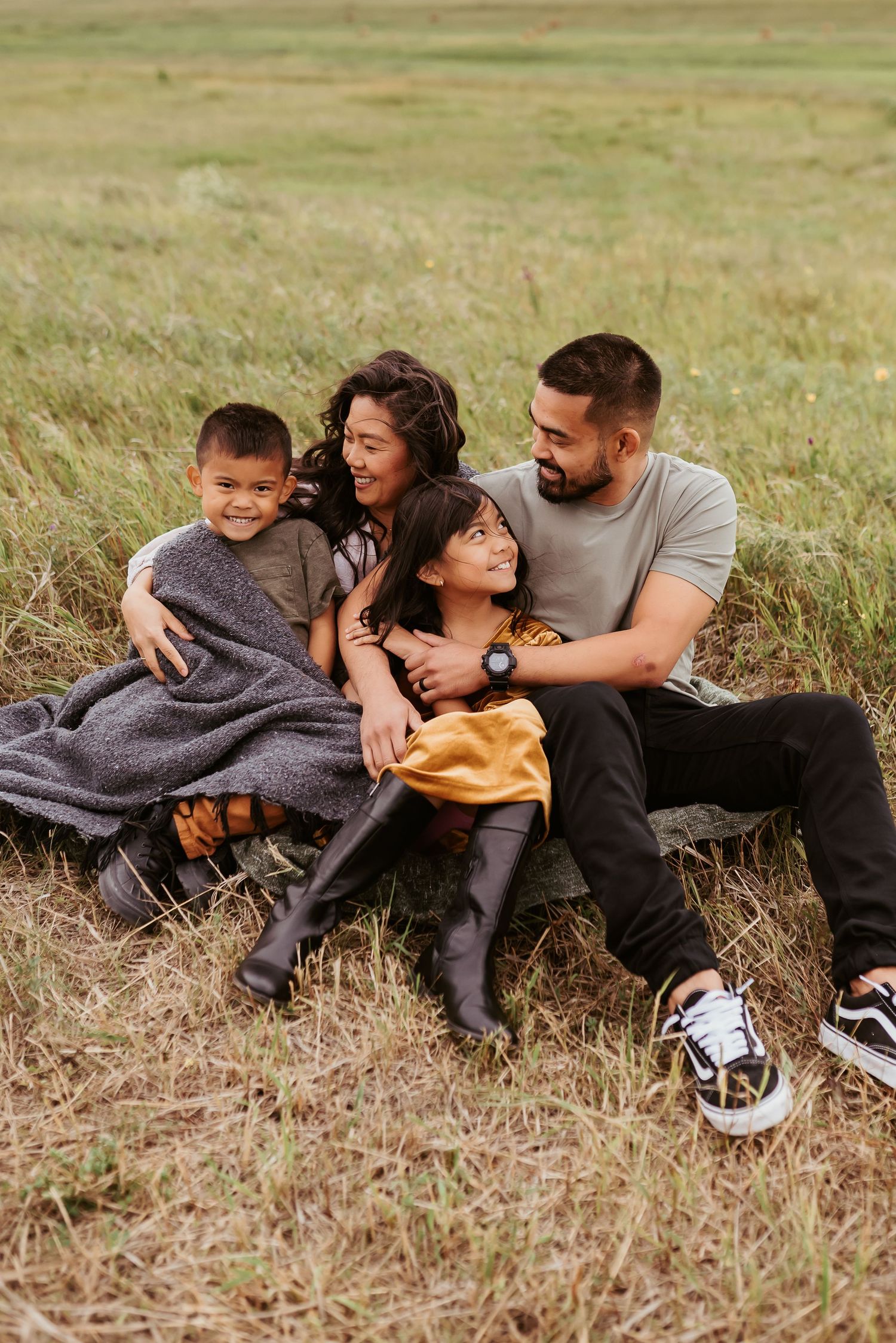 family sitting in a field on a windy day snuggling together to stay warm with smiles on their faces