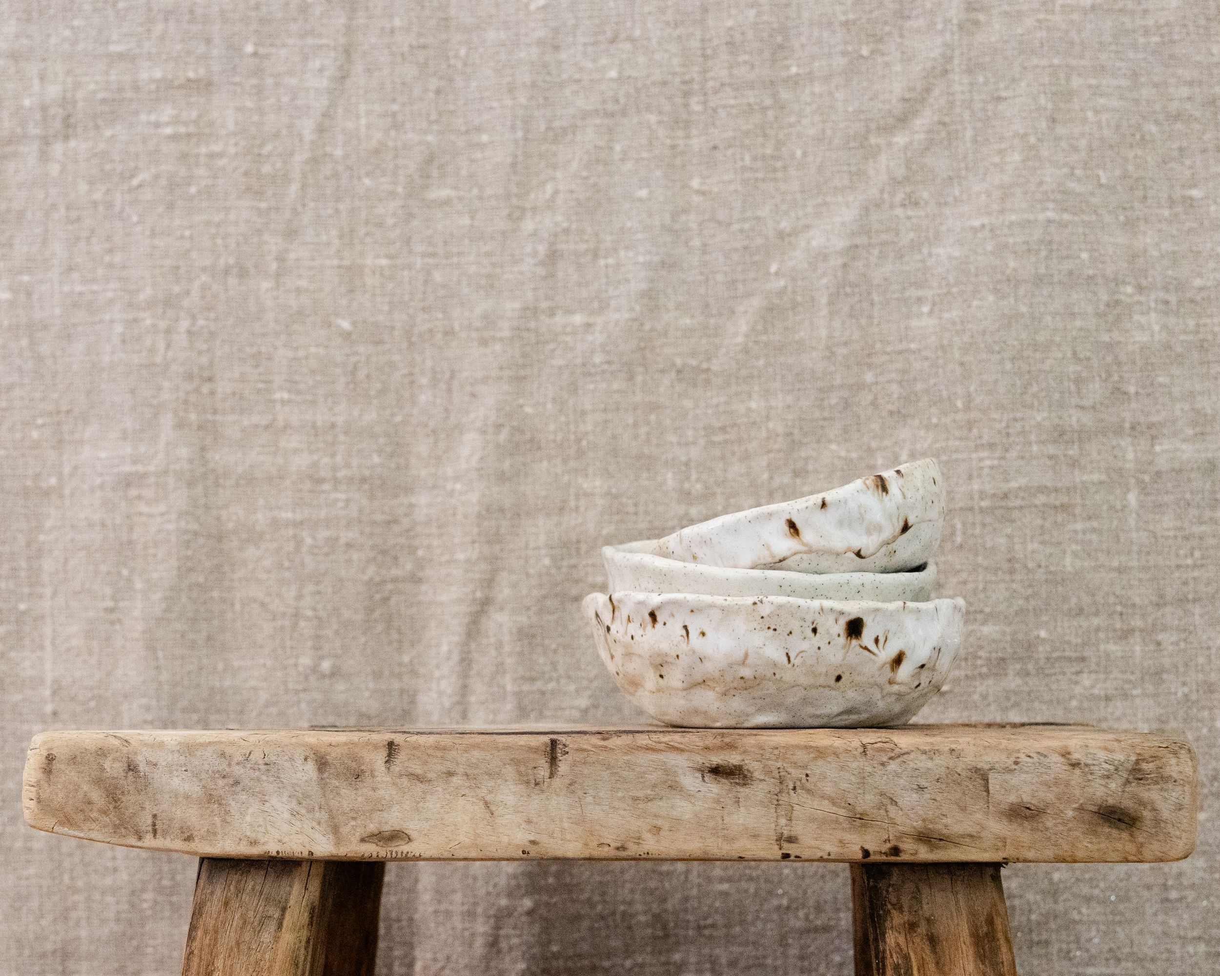 Stacked white speckled ceramic bowls displayed on a rustic wooden bench.