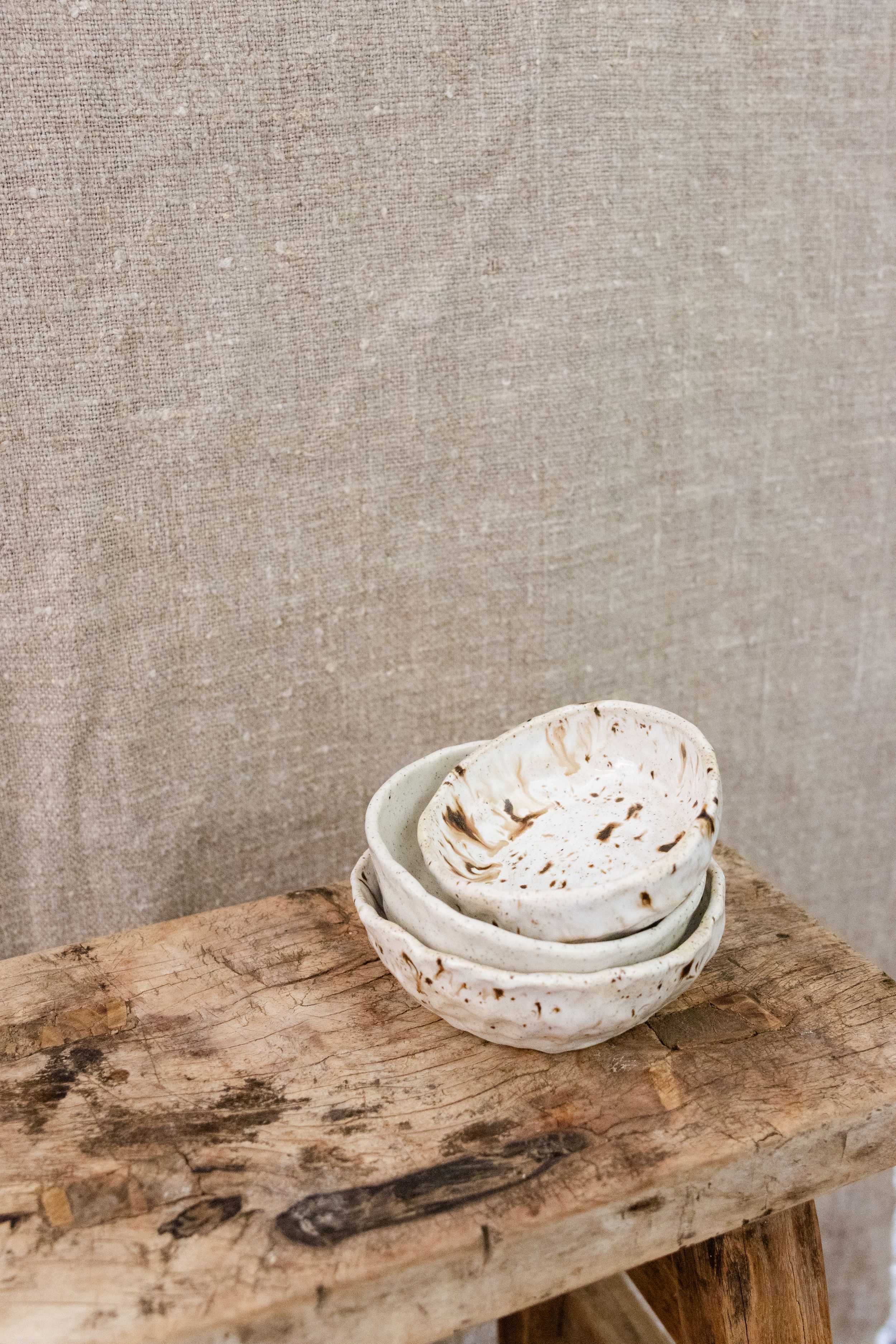 Artisanal white ceramic bowls with speckled texture stacked on weathered wooden surface.
