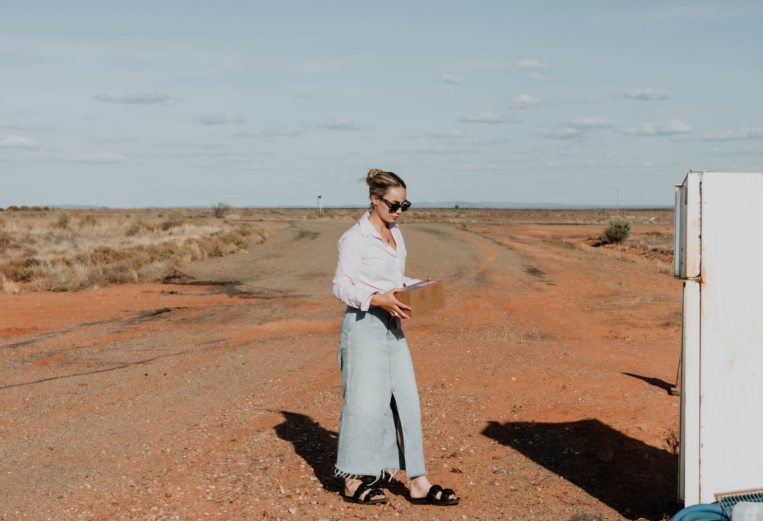 A person in white clothing stands on red desert earth near a white structure.