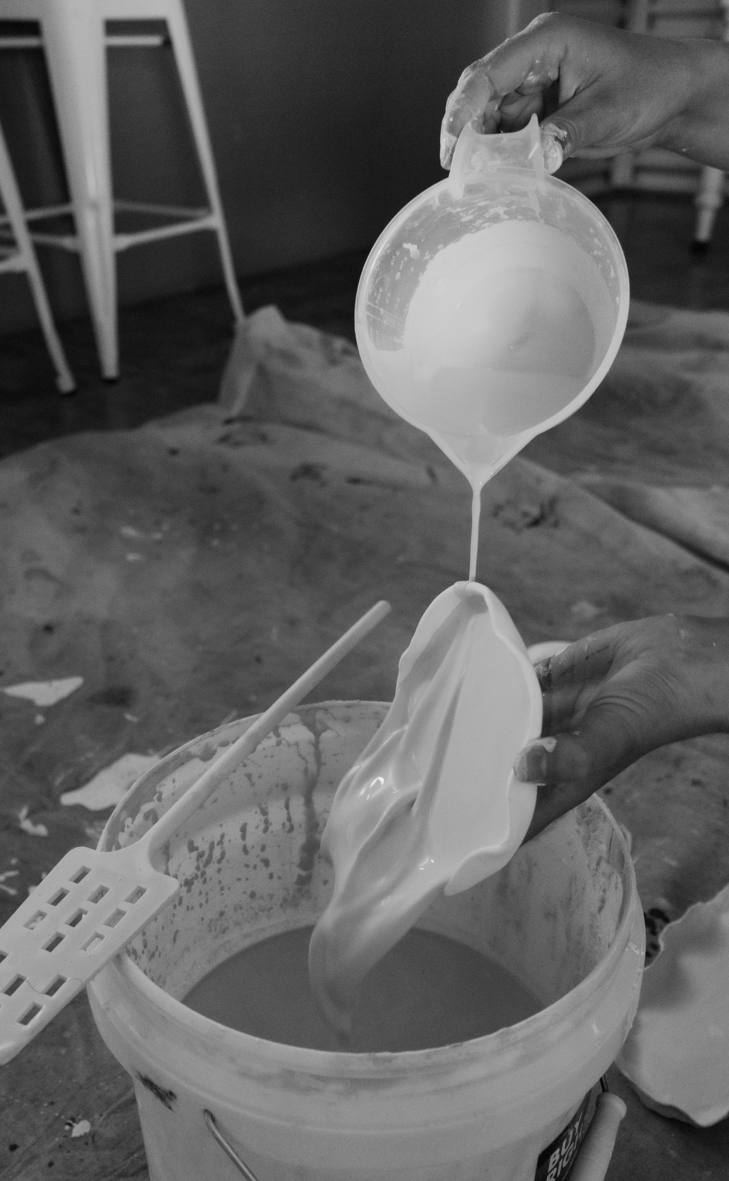 White liquid being poured from a measuring cup into a container in black and white photography.