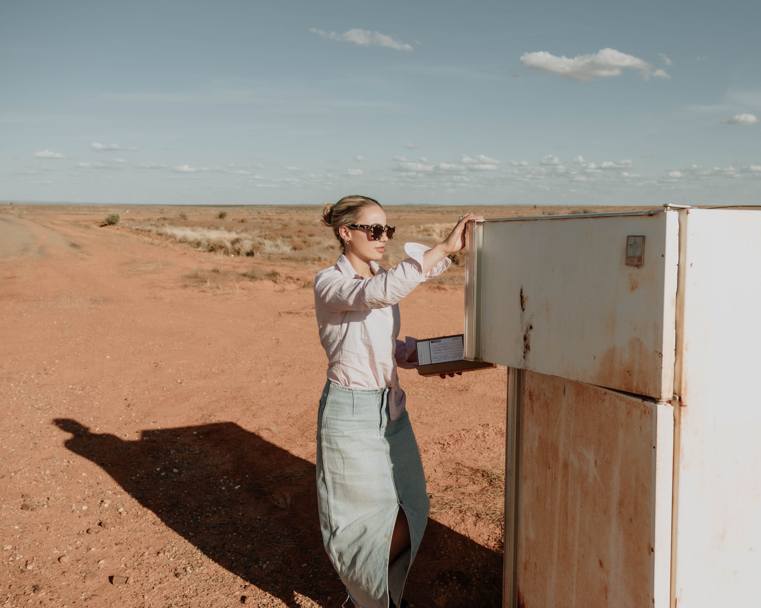 A person in light clothing opens a white cabinet door in a desert landscape.