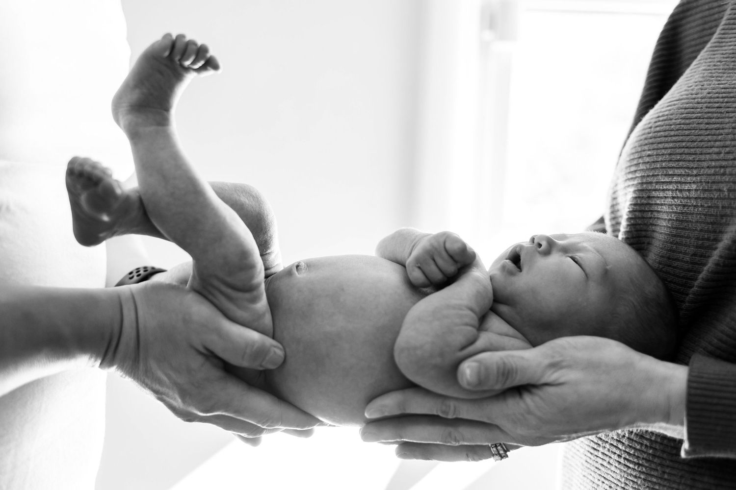 A gentle black and white photograph capturing hands holding a newborn baby during a tender moment.