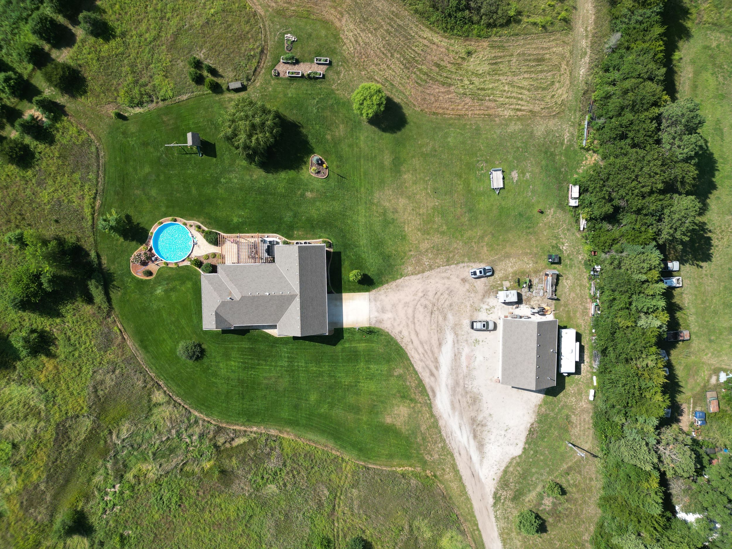 Aerial view of rural property with green lawns, buildings, and a swimming pool.