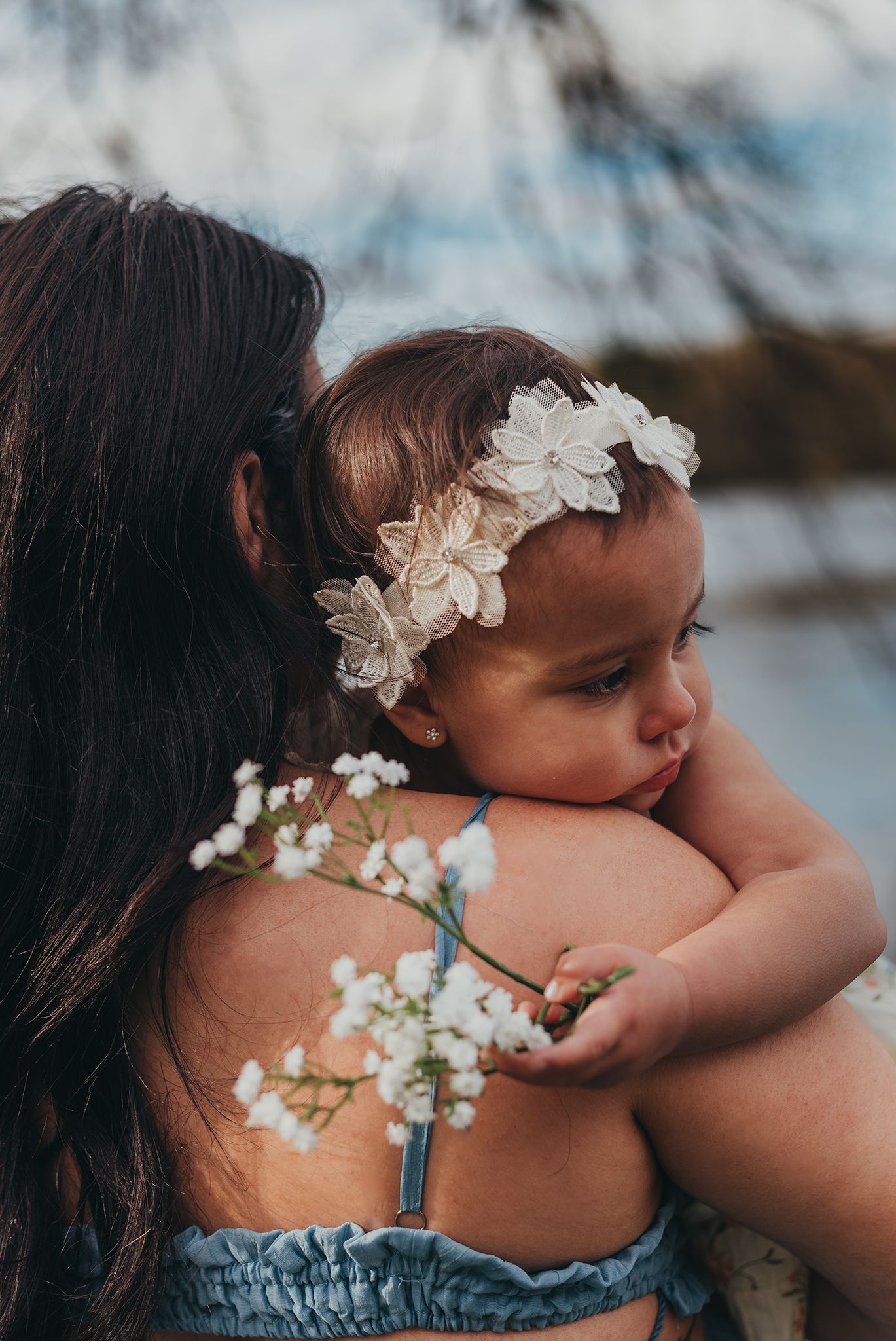 baby laying her head on mothers shoulder while holding flowers