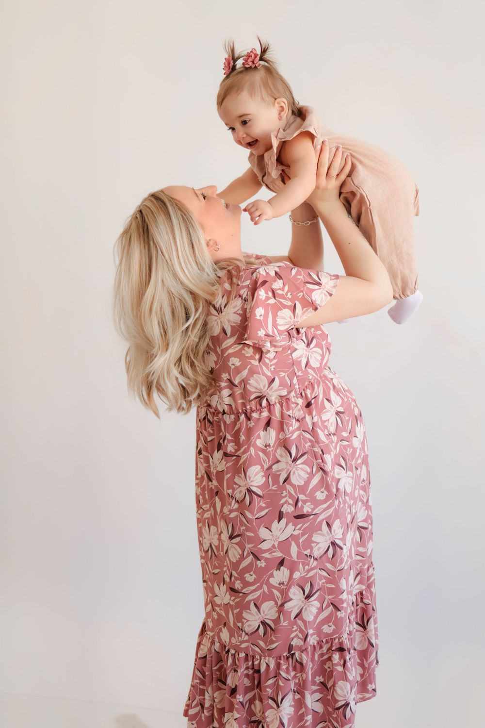 Woman in pink floral dress playing and posing with baby in matching outfit.