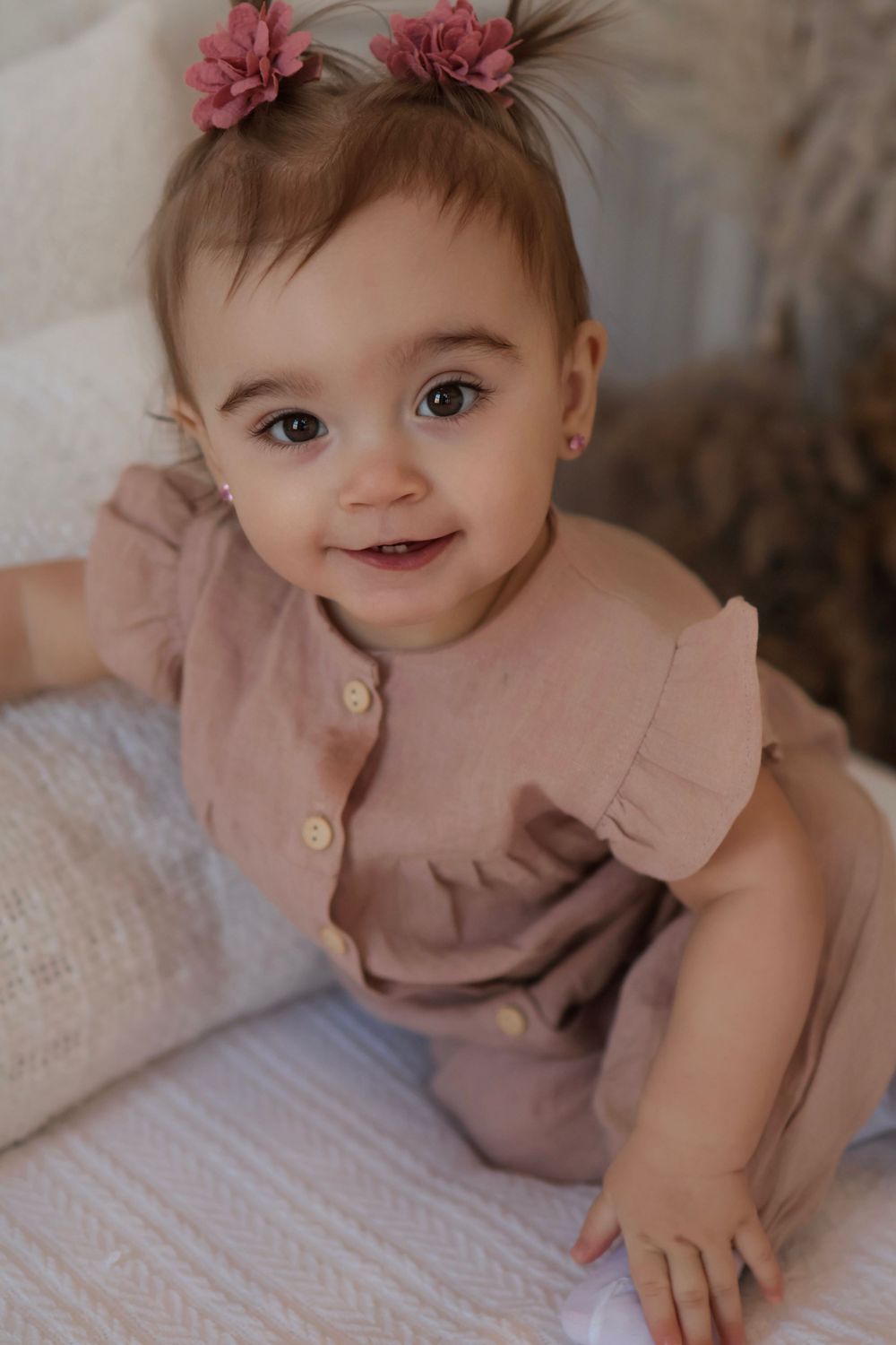 Baby wearing pink dress with floral hair accessory lying on white textured surface.