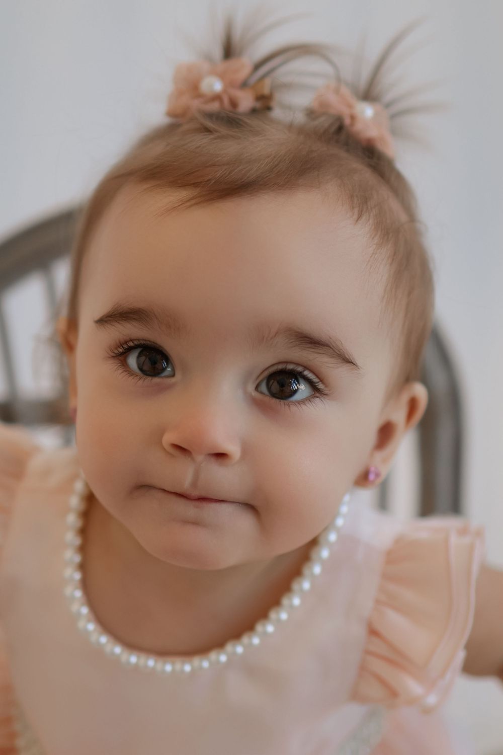 Close-up portrait of baby wearing pearl necklace and pink dress.