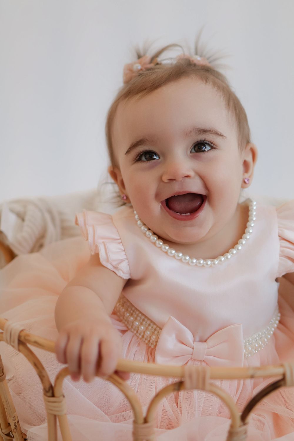 Smiling baby in pink dress and pearls sitting in woven basket.