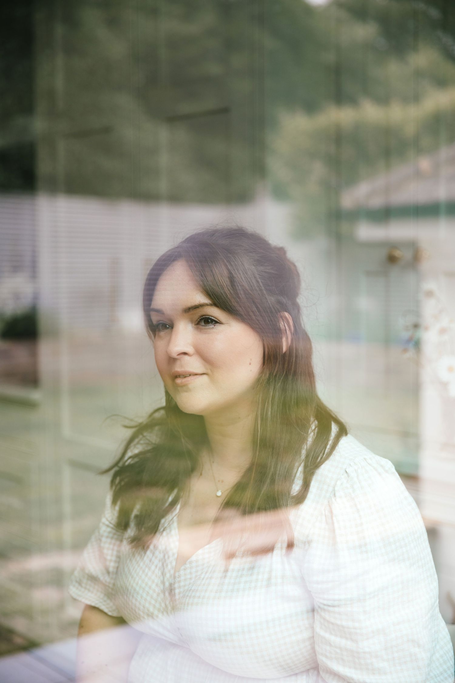 Portrait of photographer Katie Rhona Photography taken through a window wearing gingham dress
