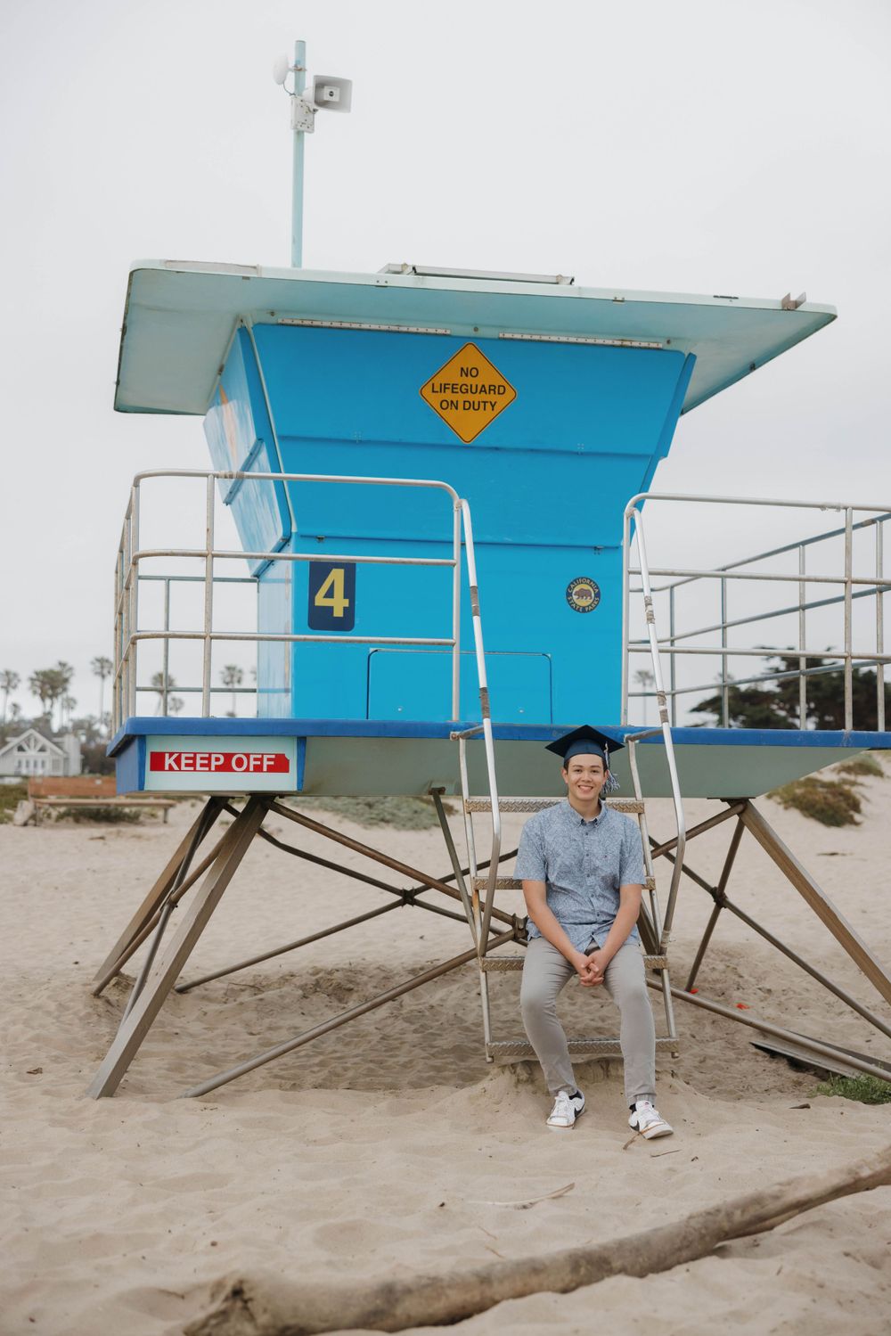 A bright blue lifeguard tower number 4 stands on the beach with someone sitting below on a cloudy day.