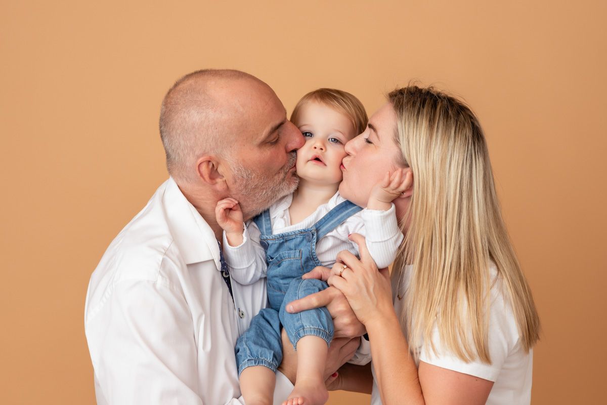 Mum and Dad kissing one year old baby girl