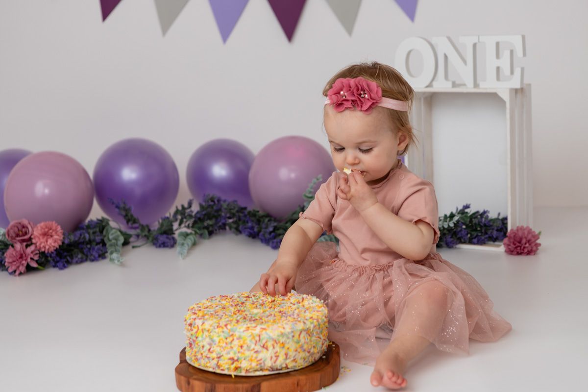 One-year-old baby sitting in front of a birthday cake with frosting on their hands