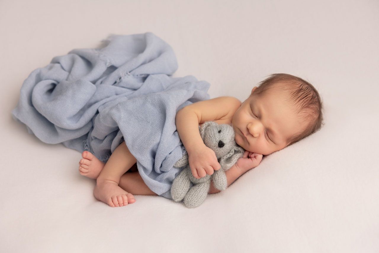newborn sleeping with a teddy and baby blue wrap