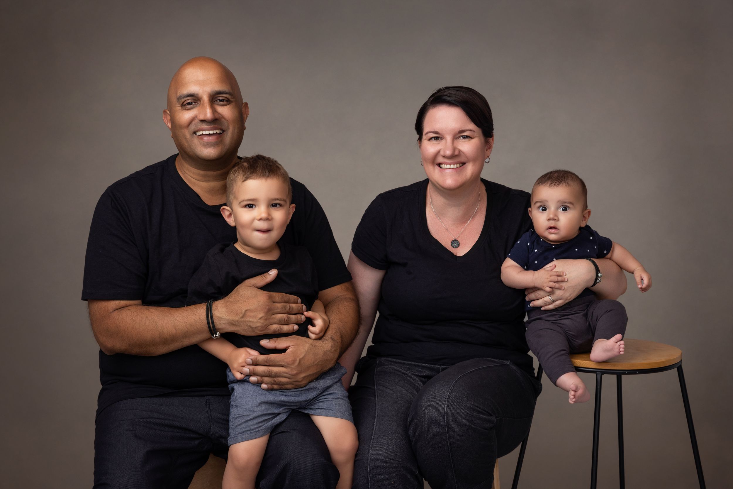 A family of four come in close for a contemporary family portrait on a textured brown background.