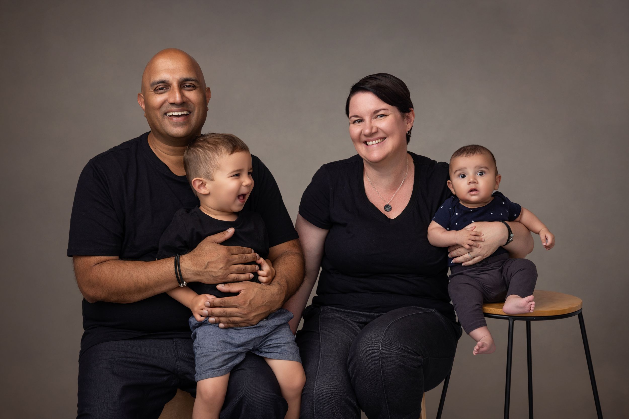 A family of four come in close for a contemporary family portrait, toddler and dad laughing.