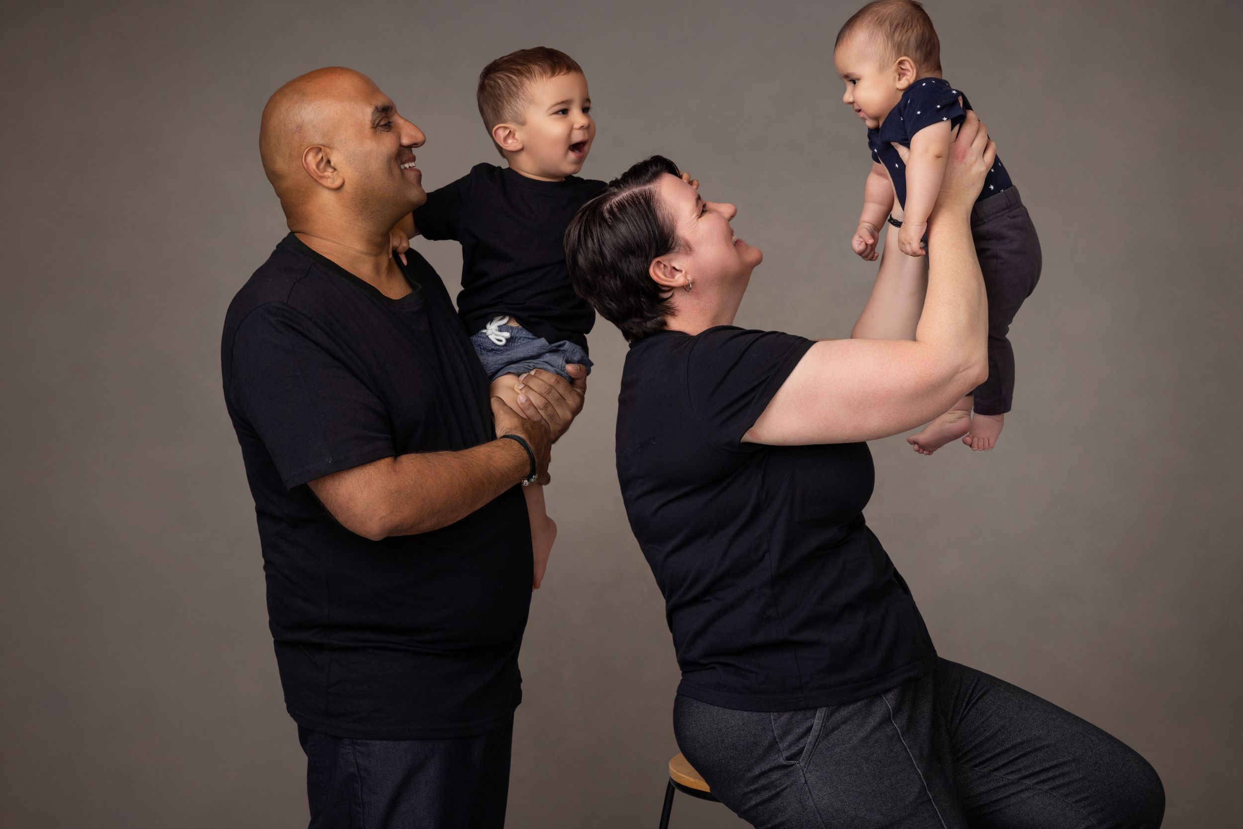 A family of four smiling and laughing as the baby gets lifted into the air.