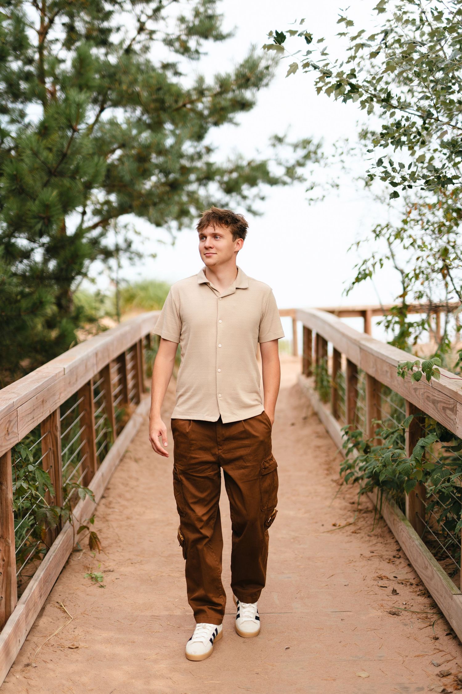 Person wearing white stands in tall grass during golden hour sunset as sunlight filters through a large tree.