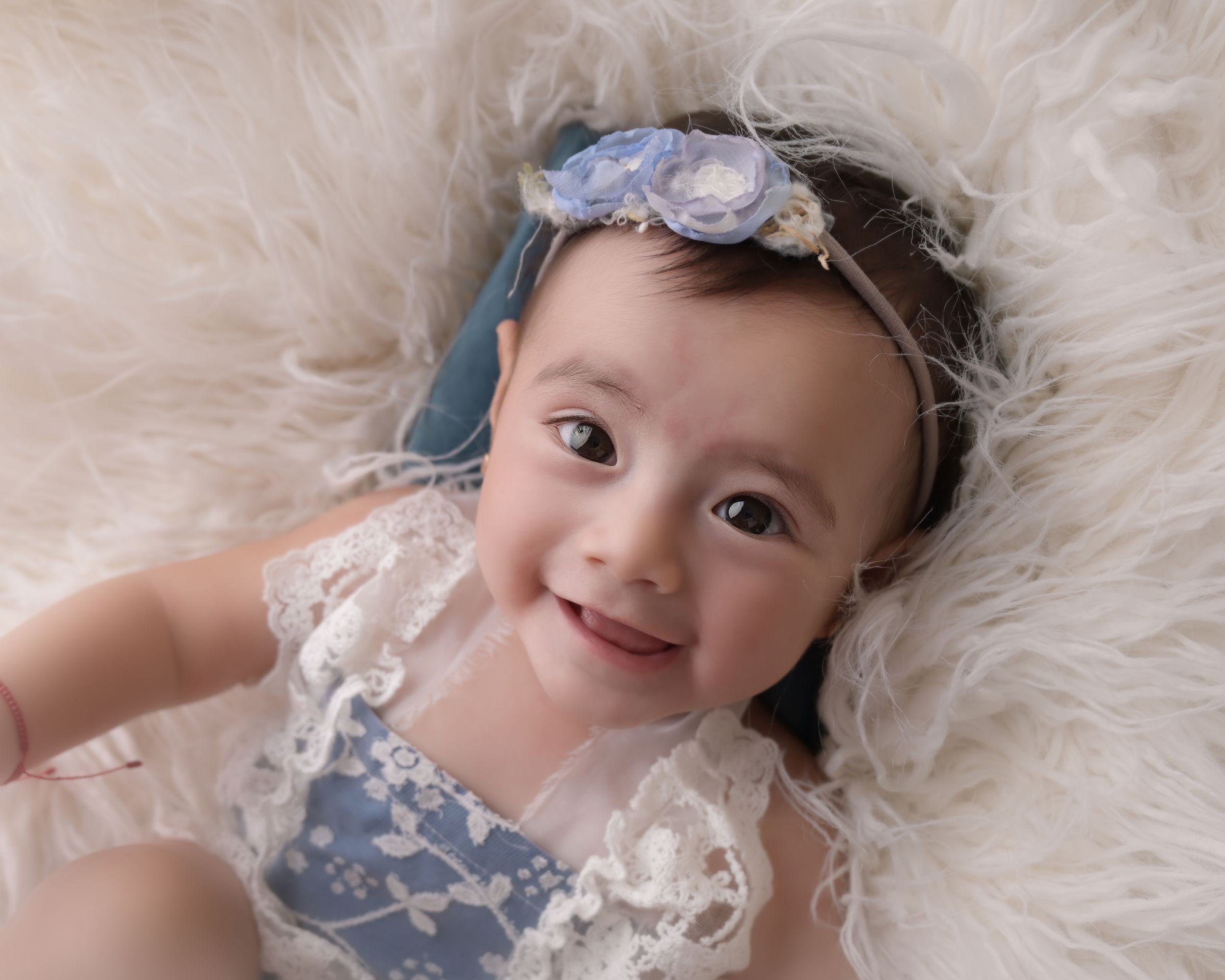 Baby portrait on white fur rug wearing blue and white outfit with headband.