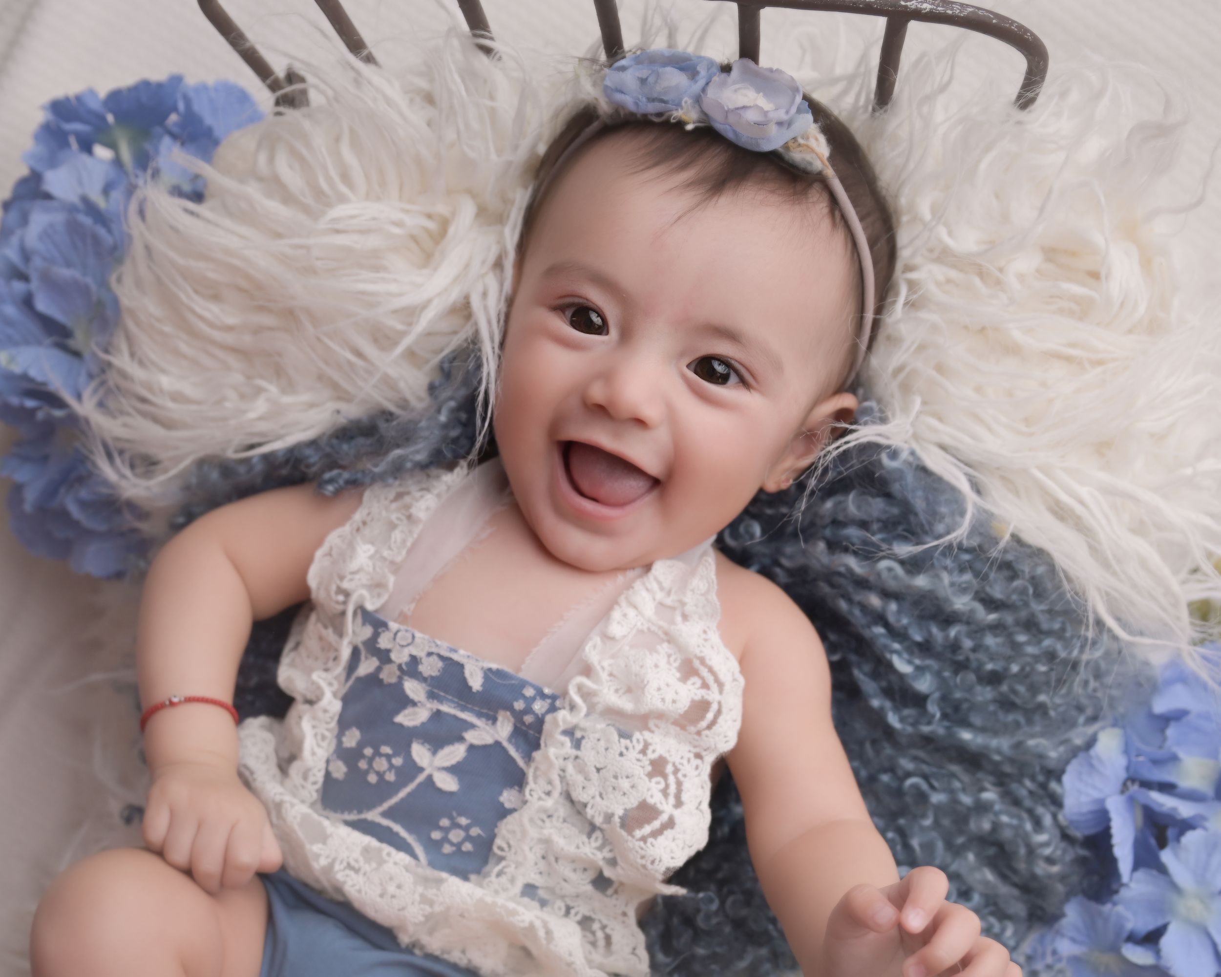 Happy baby in blue and white lace outfit lying on plush fabric with blue floral accents.