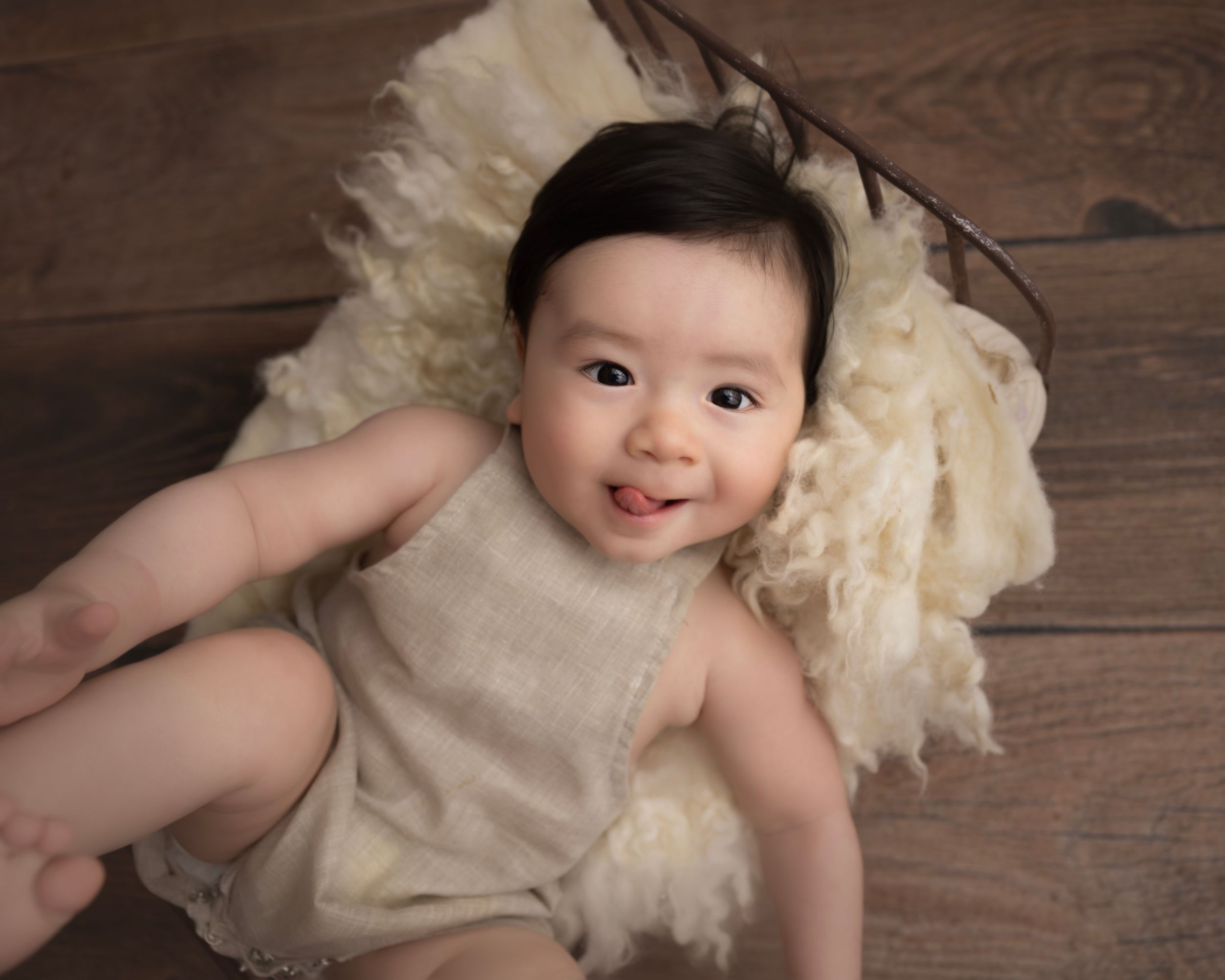 Joyful baby portrait on wooden floor with cream colored accessories.