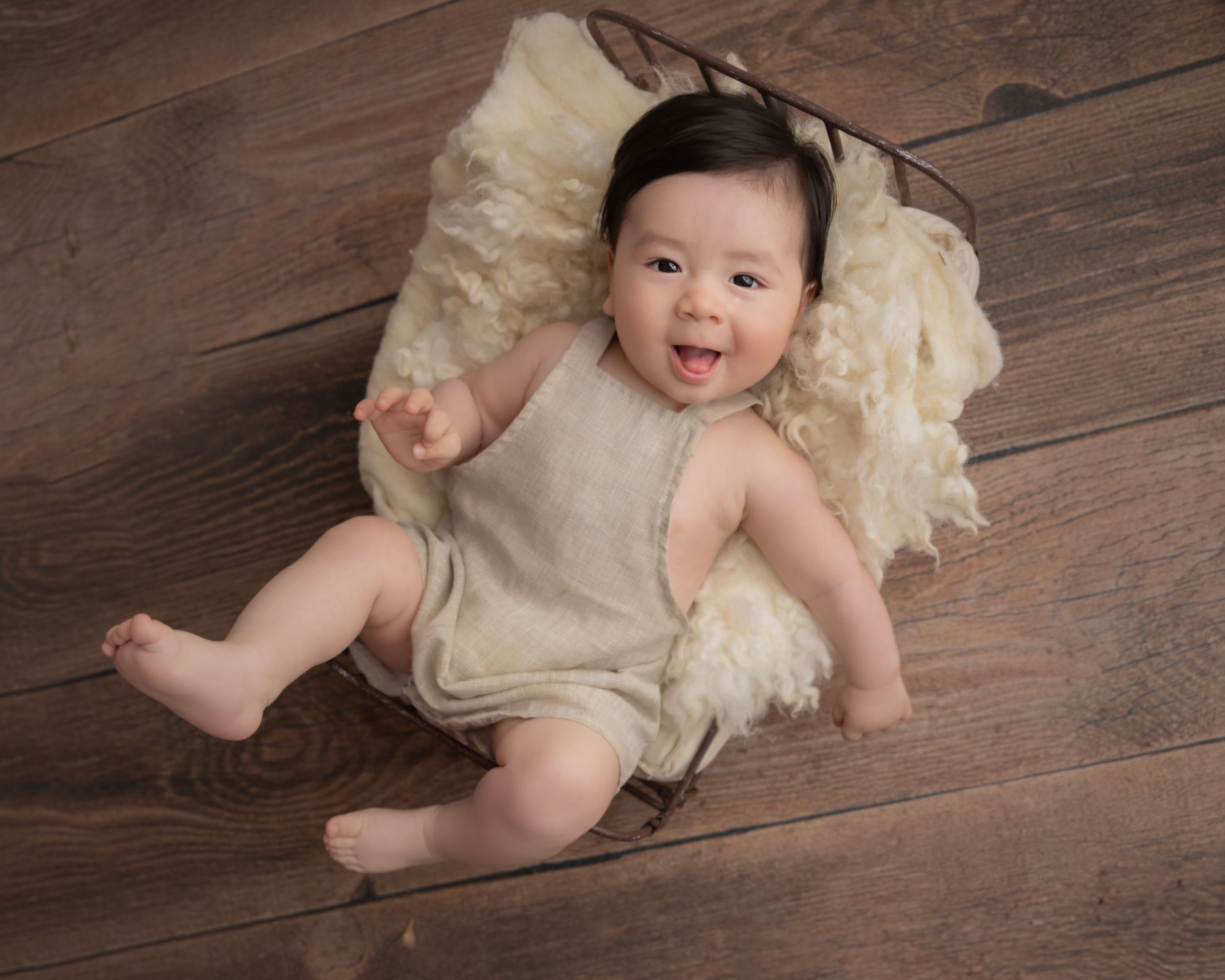Baby lying on rustic wooden floor wearing soft beige romper.