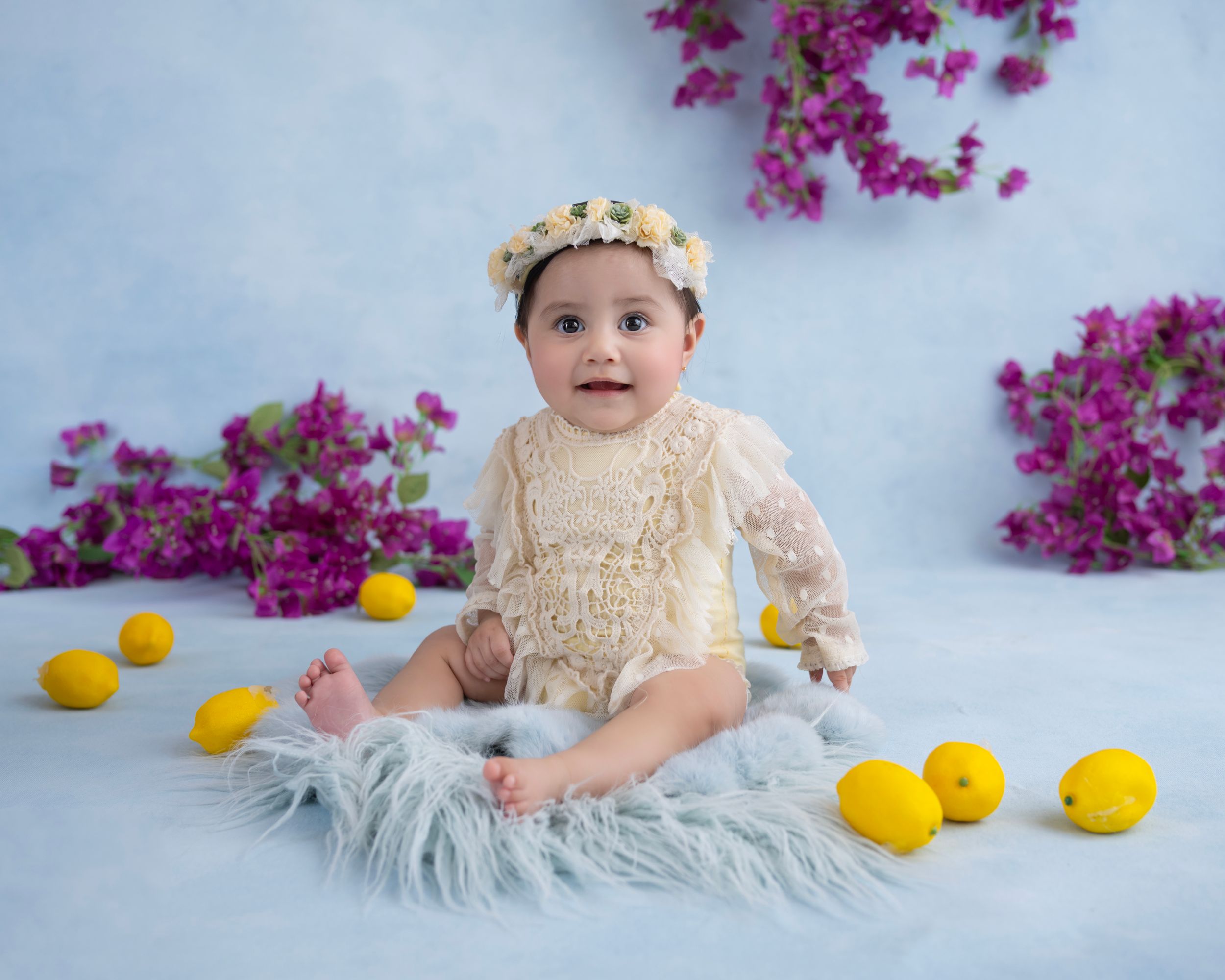 Vibrant pink flowers and yellow lemons create a whimsical backdrop for a baby photography session on soft gray fabric.