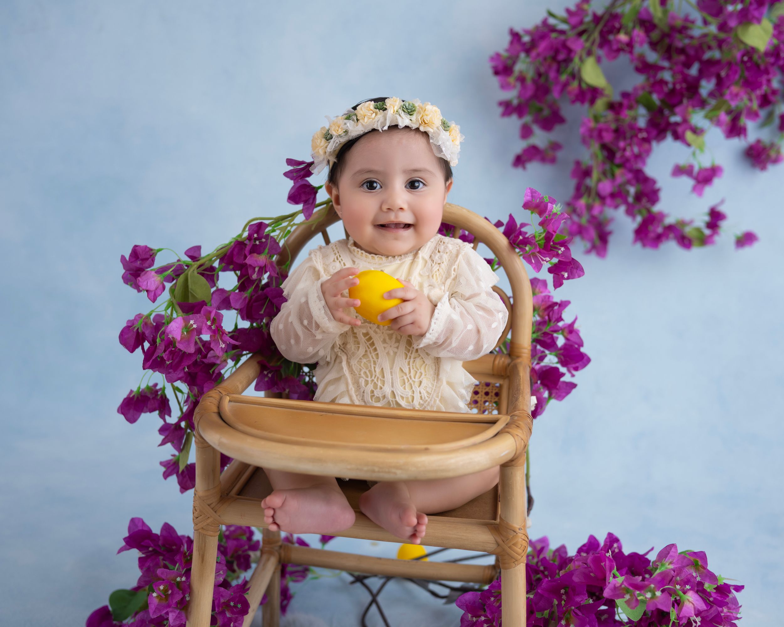Charming baby seated in wooden chair with yellow lemons and pink floral accents.