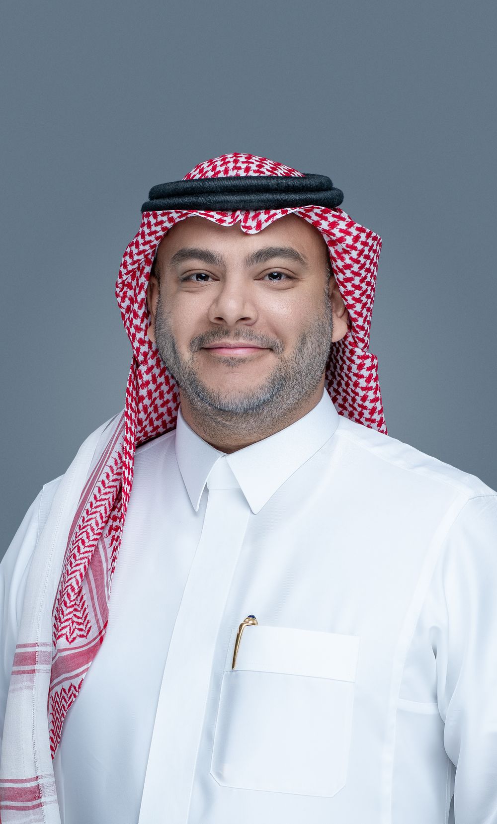 Professional headshot portrait of someone wearing traditional Middle Eastern white thobe and red and white checkered keffiyeh.
