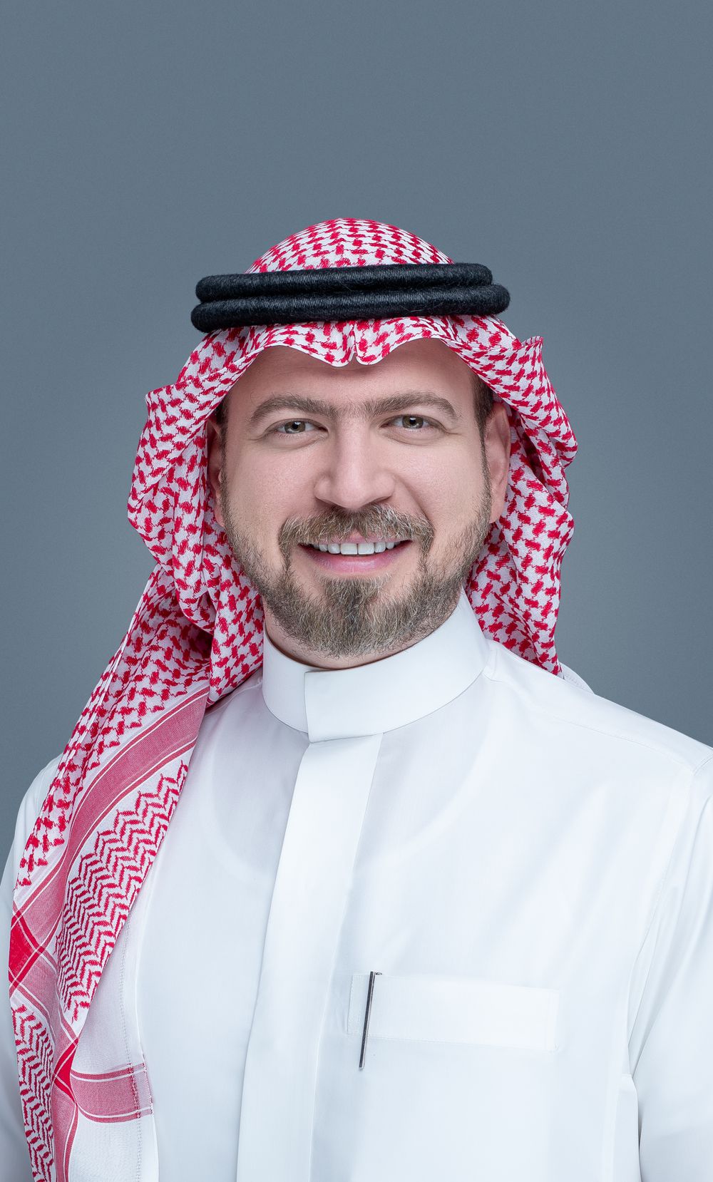A person wearing traditional Middle Eastern clothing including a red and white keffiyeh and white thobe against a gray background.