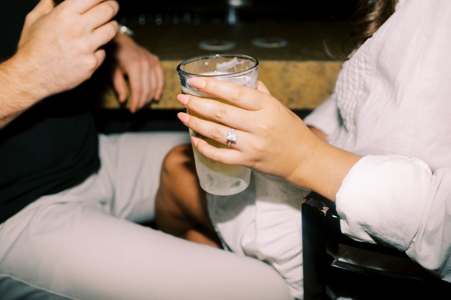 Someone holds a cocktail glass containing a creamy white beverage during a casual social gathering.