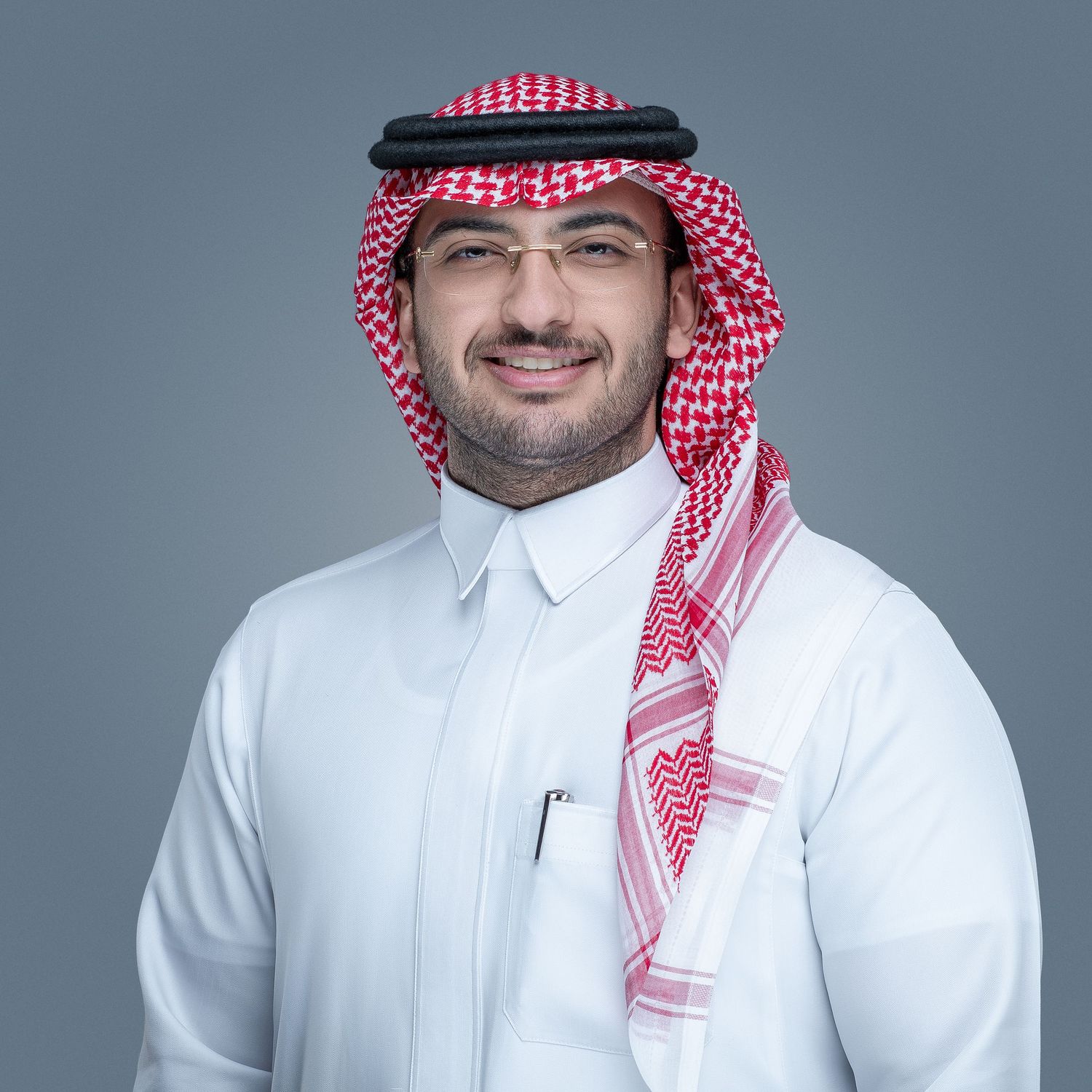 A professional headshot of a person wearing traditional Middle Eastern dress including a white thobe and red and white keffiyeh.