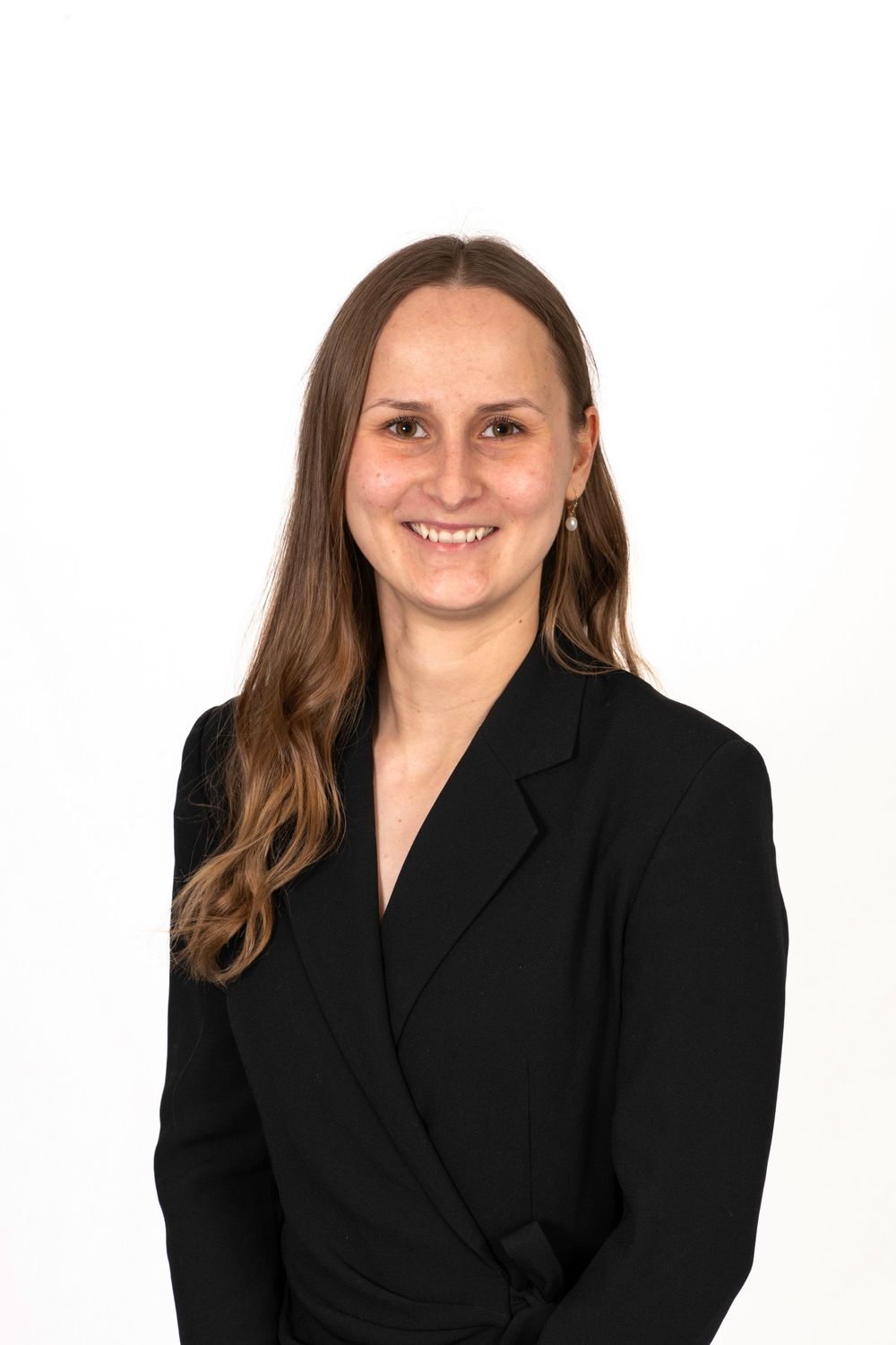 Professional headshot of a smiling woman with long brown hair wearing a black blazer against a white background.